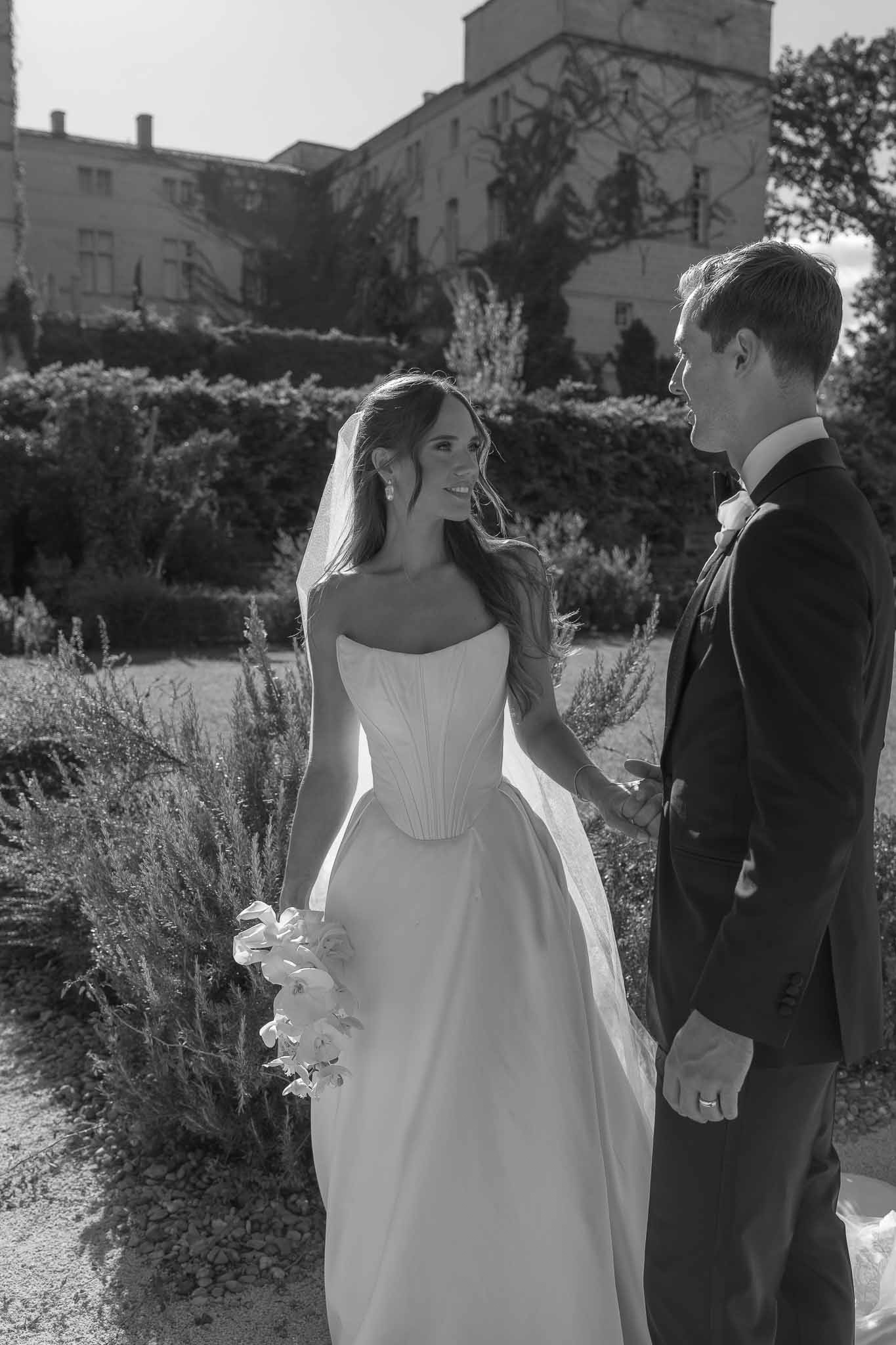 Black and white portrait of couple in formal garden with bride in corset ballgown and cathedral veil