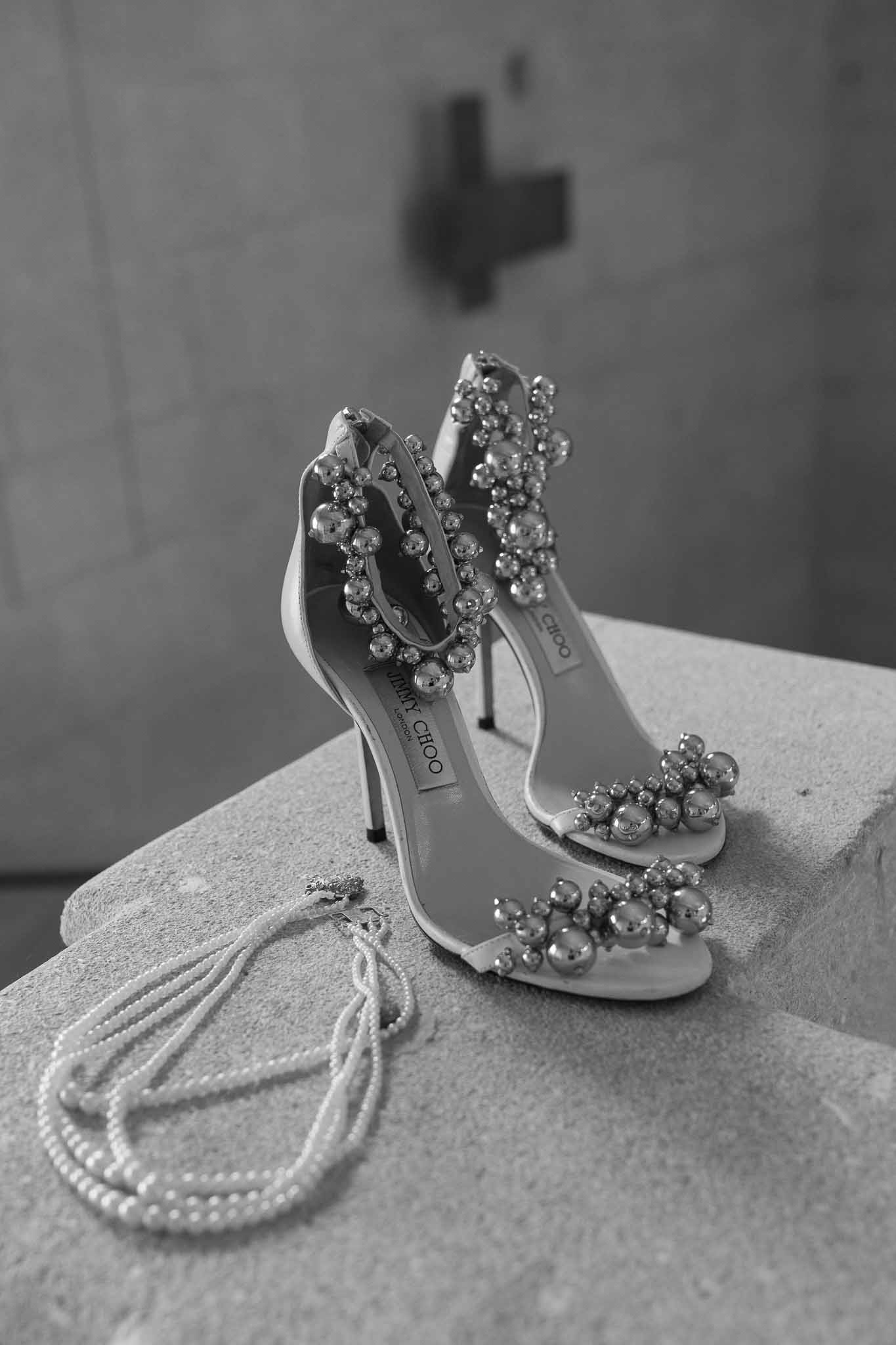 Black and white Jimmy Choo beaded stiletto sandals with pearl necklace on stone surface