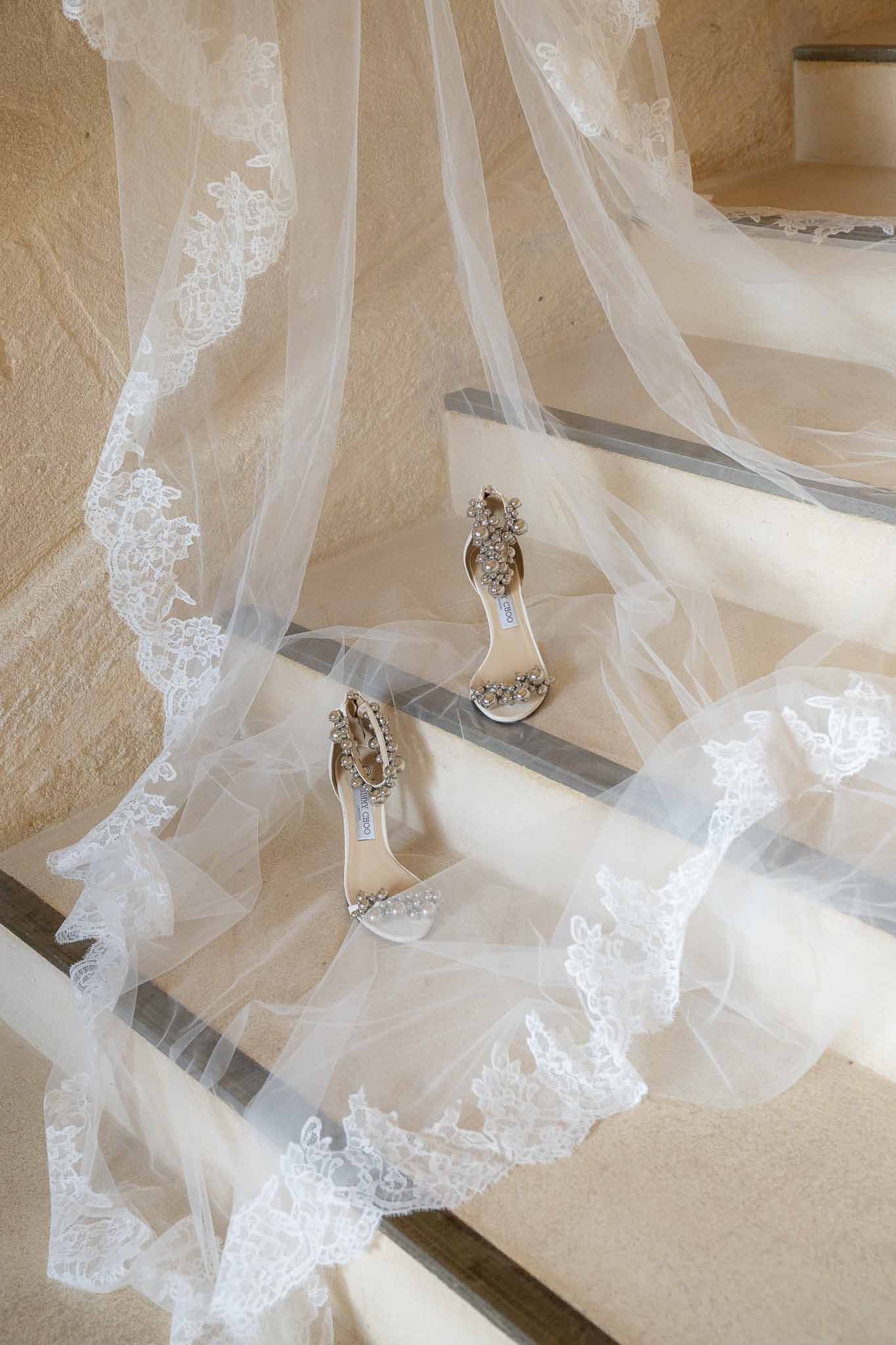 Jimmy Choo pearl-embellished bridal sandals arranged on stone stairs with lace-trimmed cathedral veil