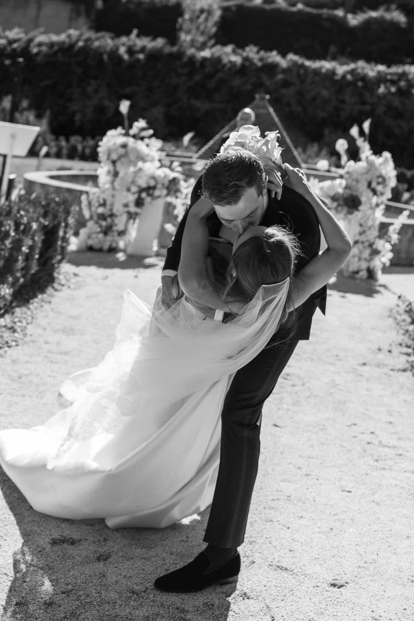 Black and white dramatic dip kiss at outdoor garden ceremony with floral arch behind