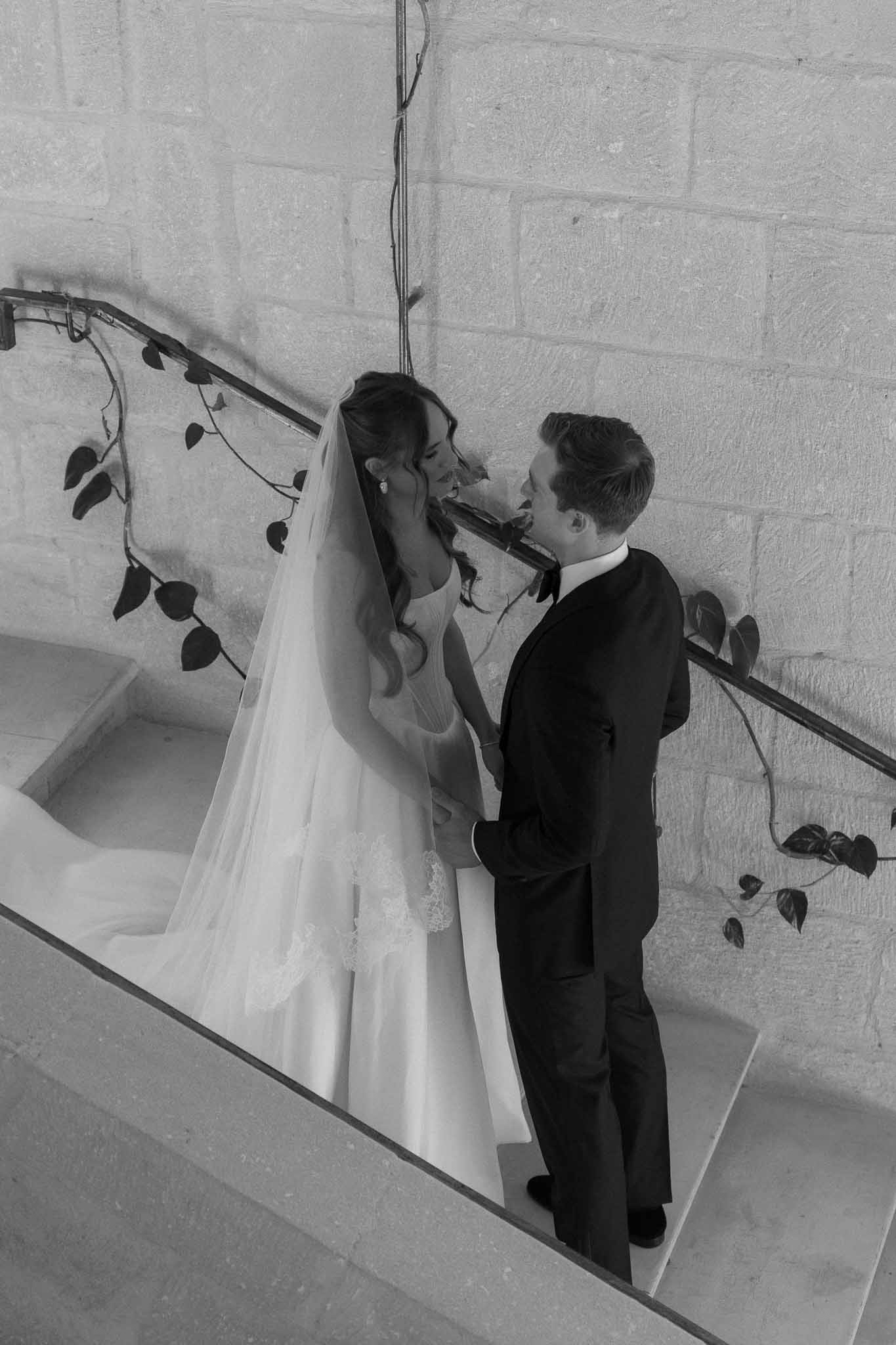 Black and white overhead couple kissing on stone staircase bride in lace ball gown with cathedral veil