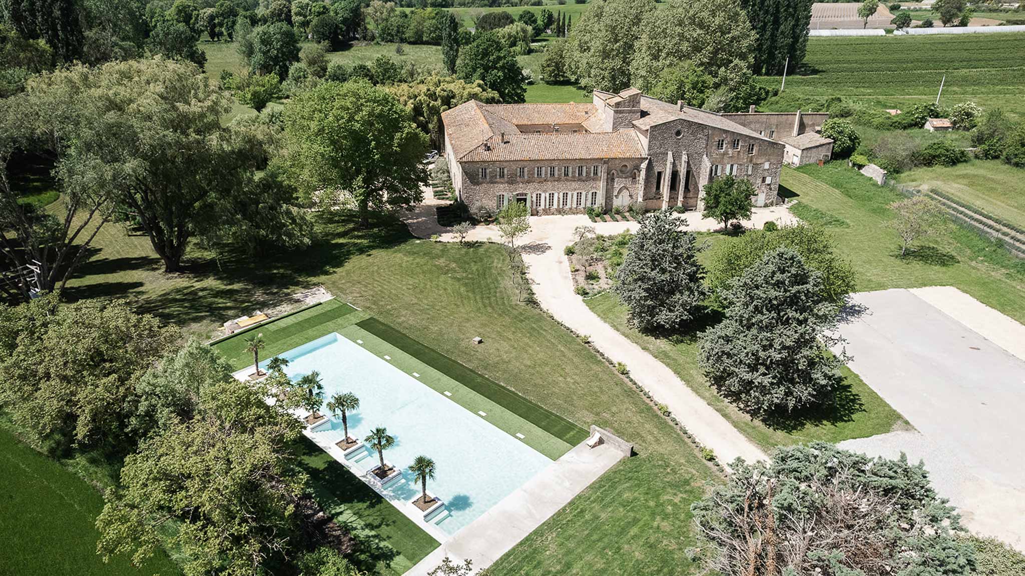 Aerial view of stone manor house with terracotta roof, swimming pool, manicured lawns, and surrounding vineyards
