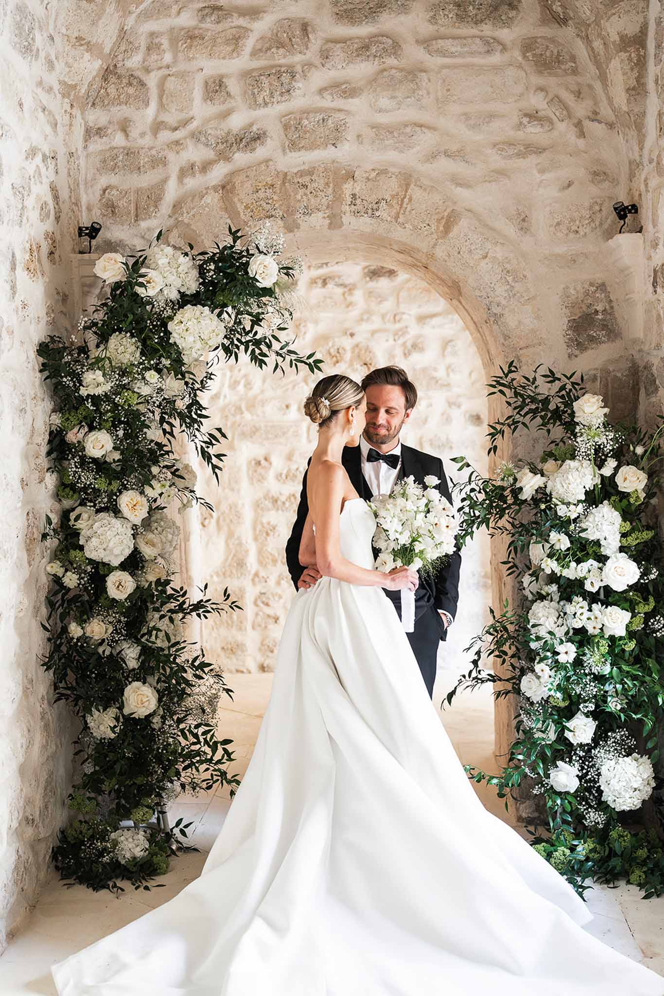 Couple framed by circular white rose and hydrangea arch inside vaulted stone archway