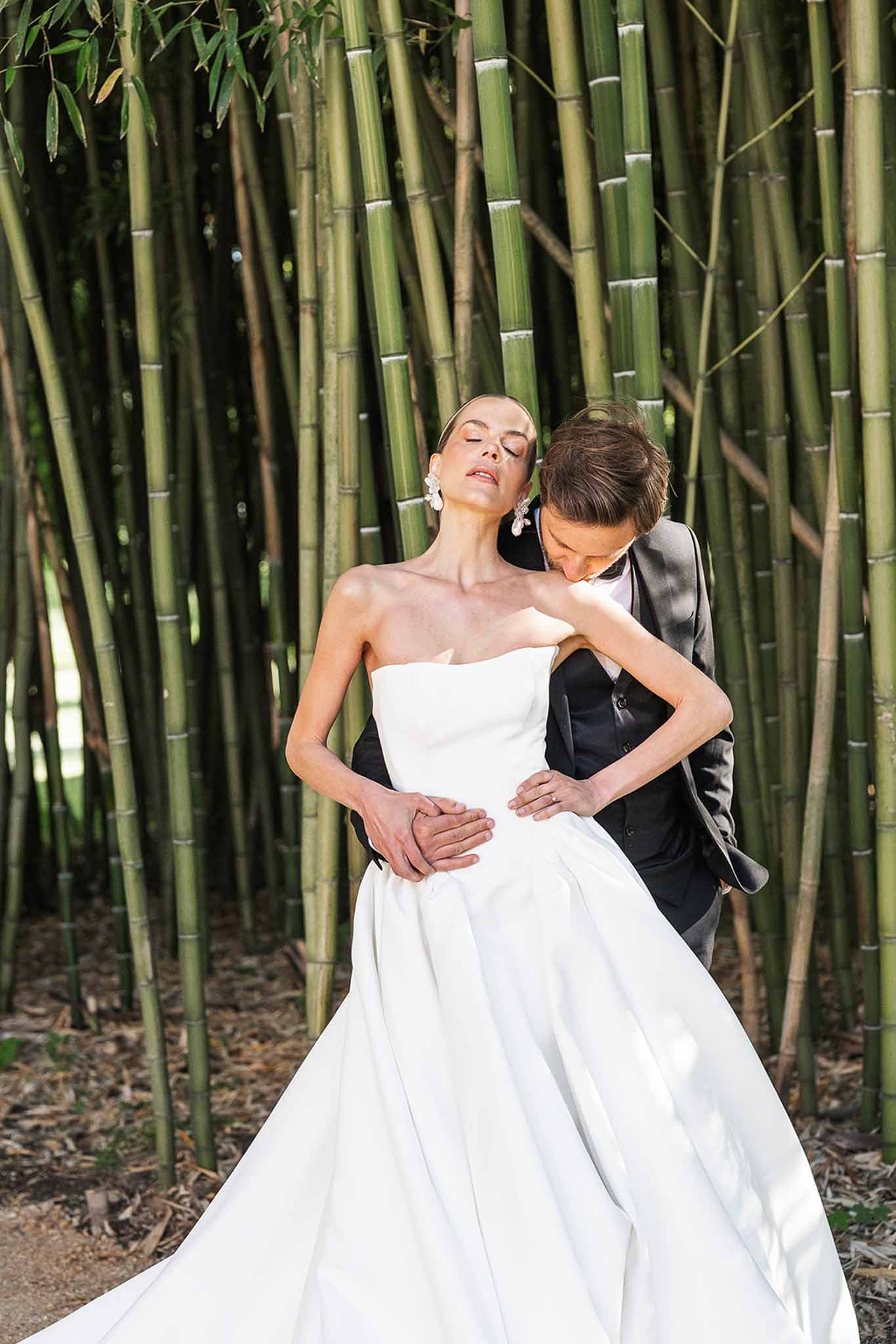 Groom kissing brides shoulder in bamboo grove bride in strapless pleated ballgown with crystal drop earrings
