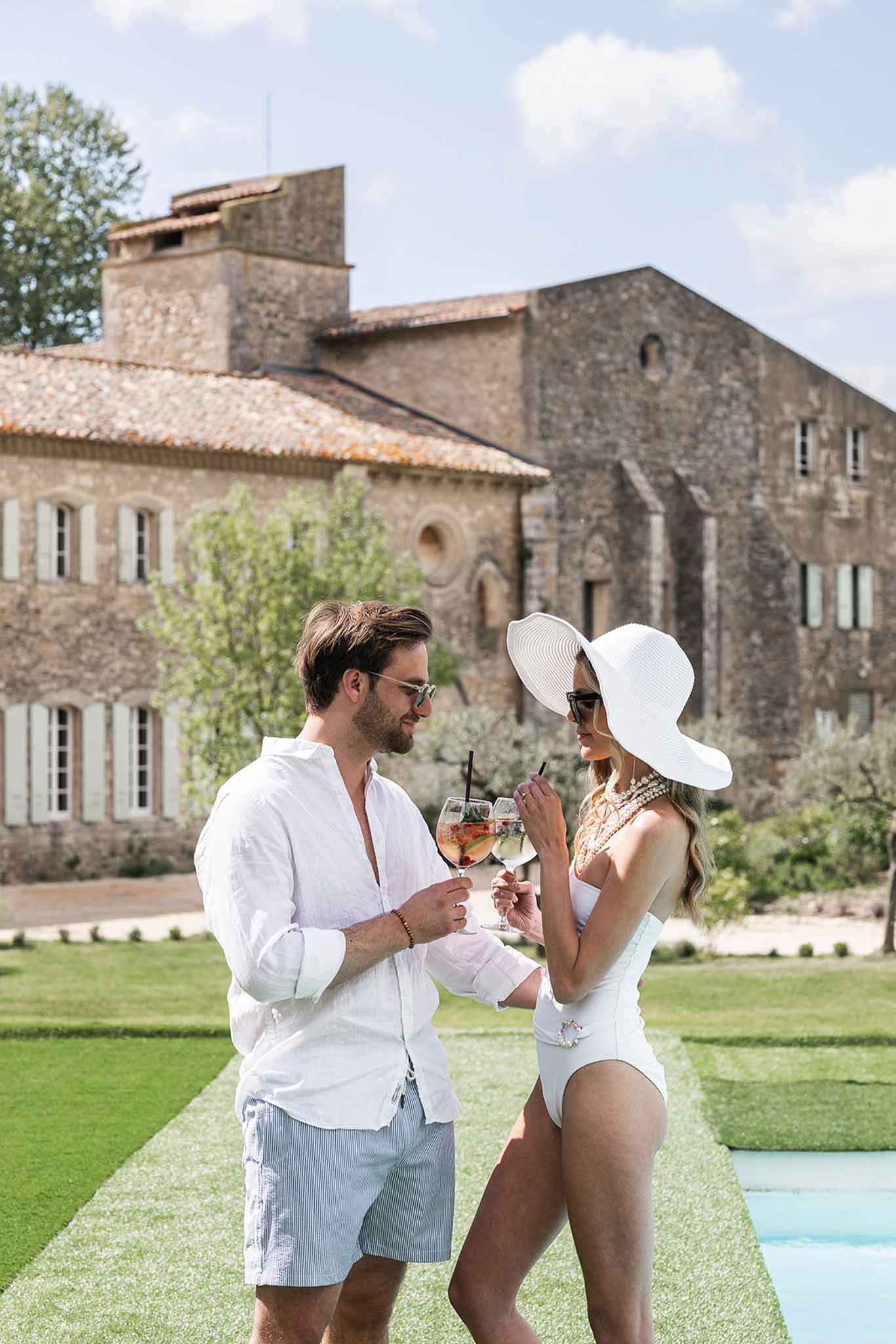 Couple in swimwear clinking spritz cocktails poolside at stone chateau abbey venue