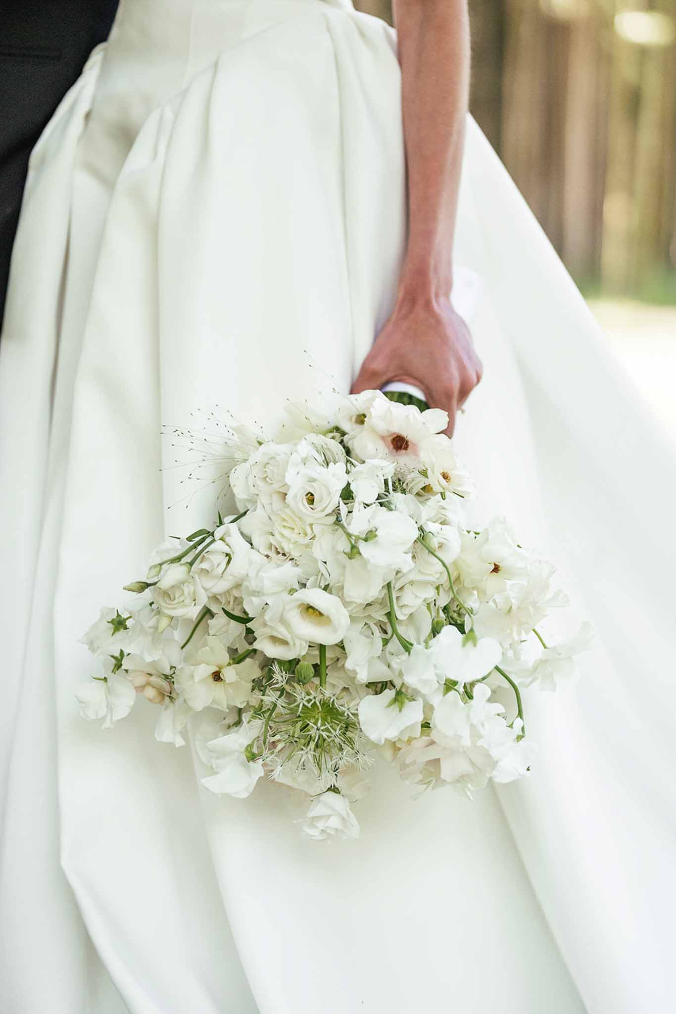 Close-up of bride holding a loose white and cream bouquet of ranunculus, anemones, and sweet peas