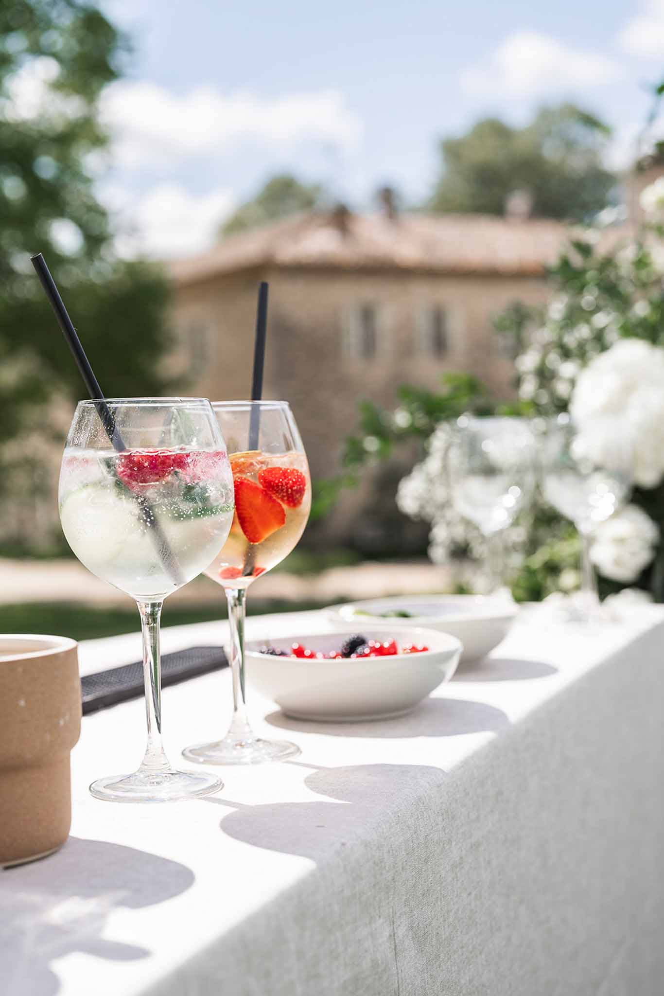 Two balloon wine glasses with berries and mint beside ceramic bowls on white linen at stone manor