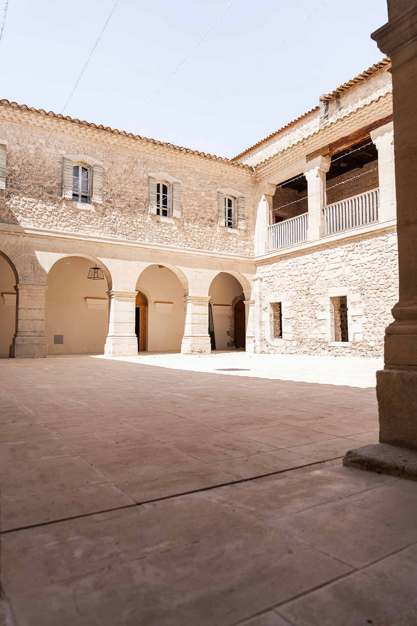 Stone courtyard of historic French building with arched arcade, wrought-iron balcony, and fairy lights
