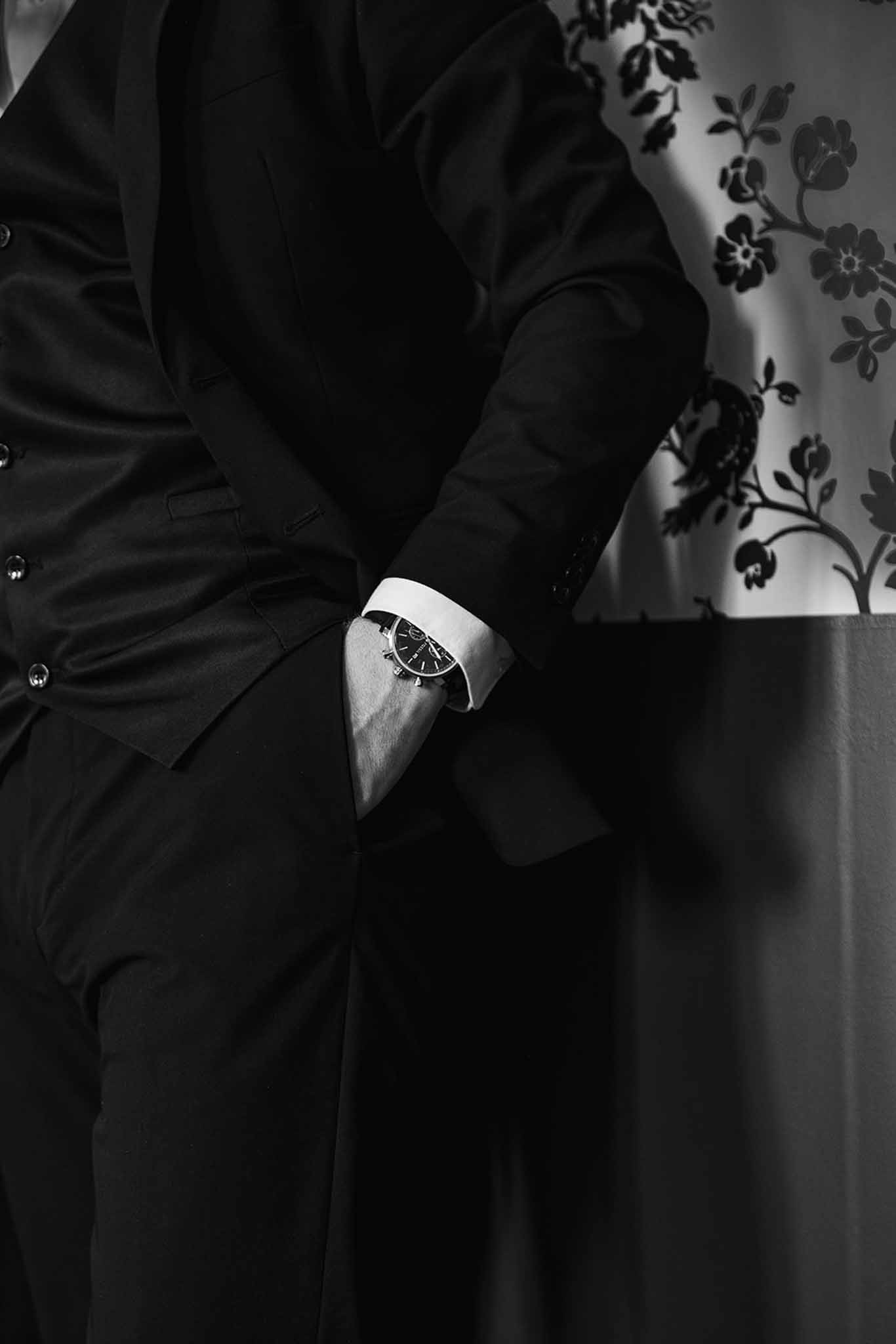 Black and white close-up of groom's watch and double-breasted suit jacket with hand in pocket
