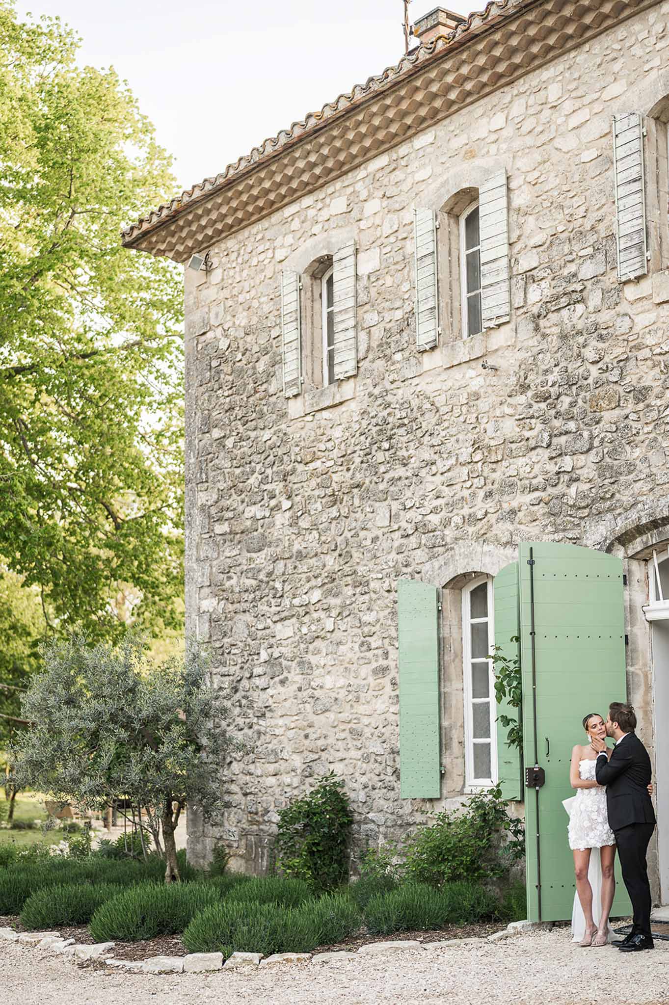 Couple sharing intimate moment beside sage green door of Provencal stone farmhouse with limestone walls