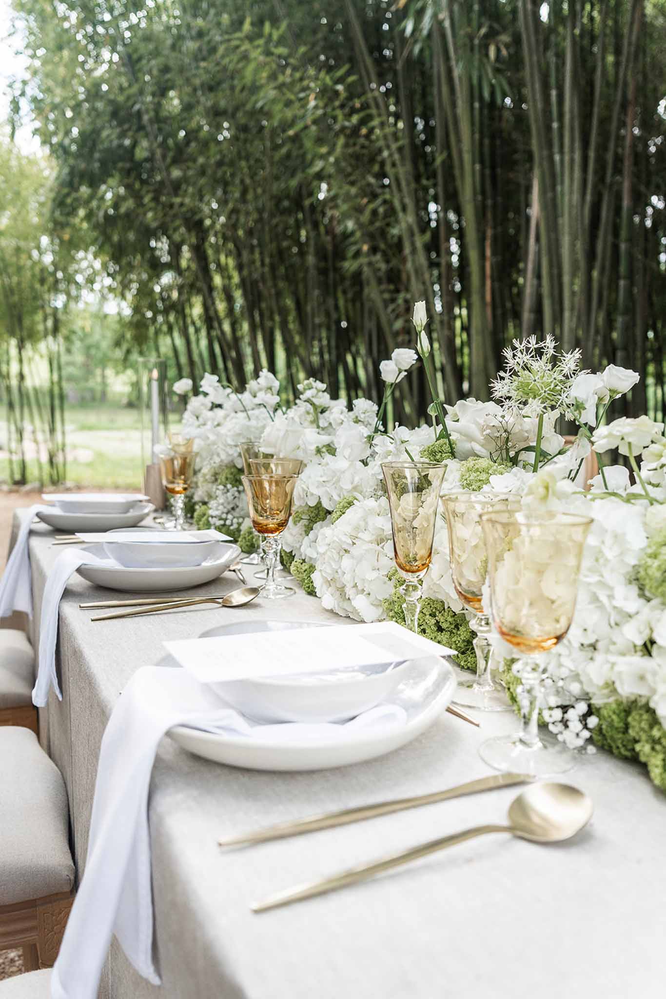 Close-up of reception table with white hydrangea floral runner, gold flatware, and amber glassware