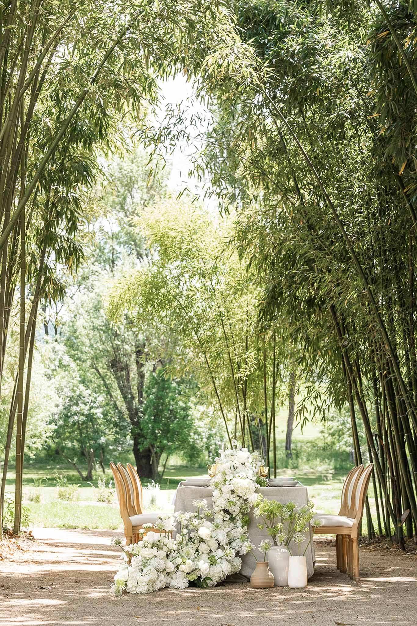Sweetheart table with white hydrangea and rose floral runner on gravel path between bamboo groves