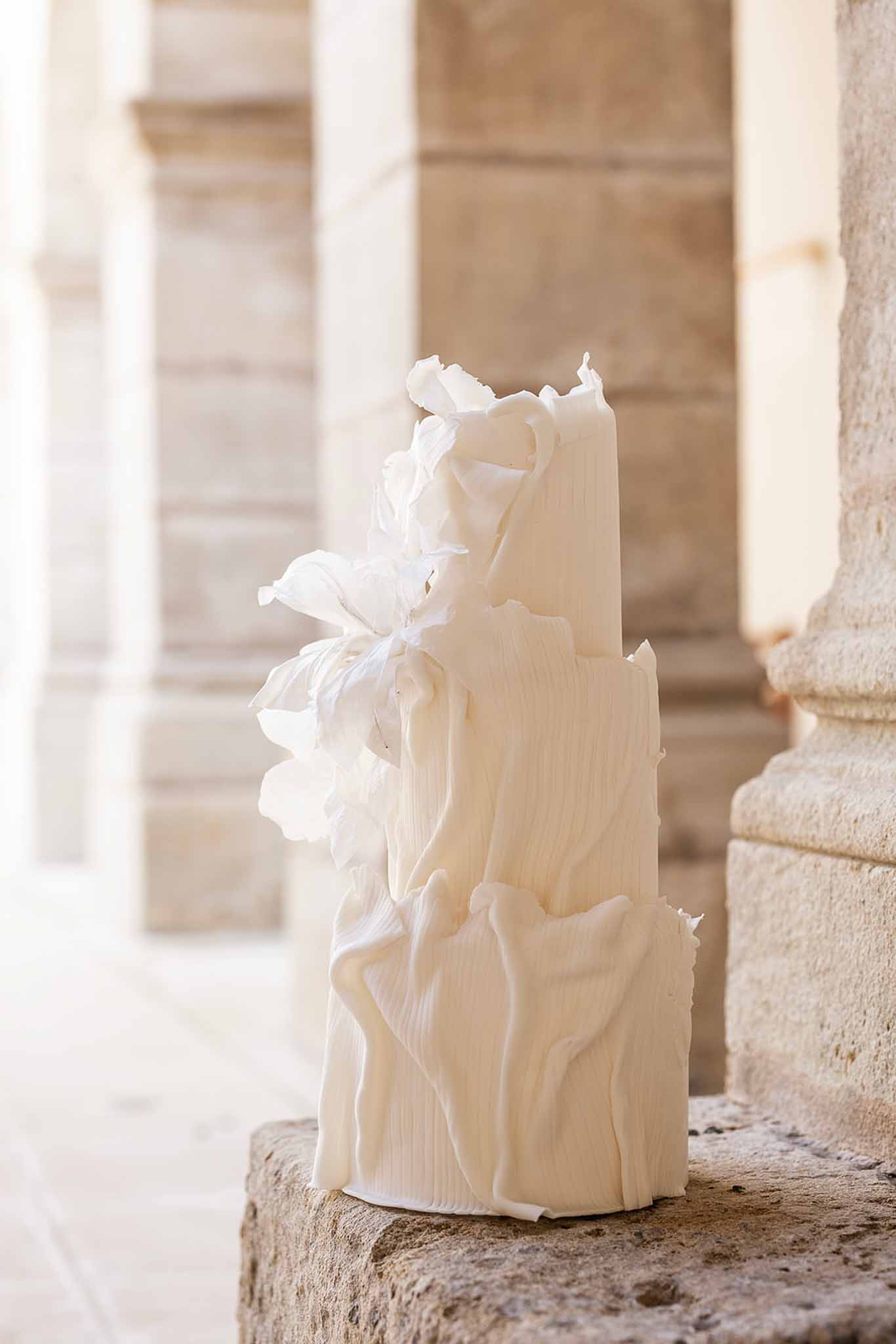 Sculptural ivory wedding cake with ruffled fondant and white sugar flowers against stone columns