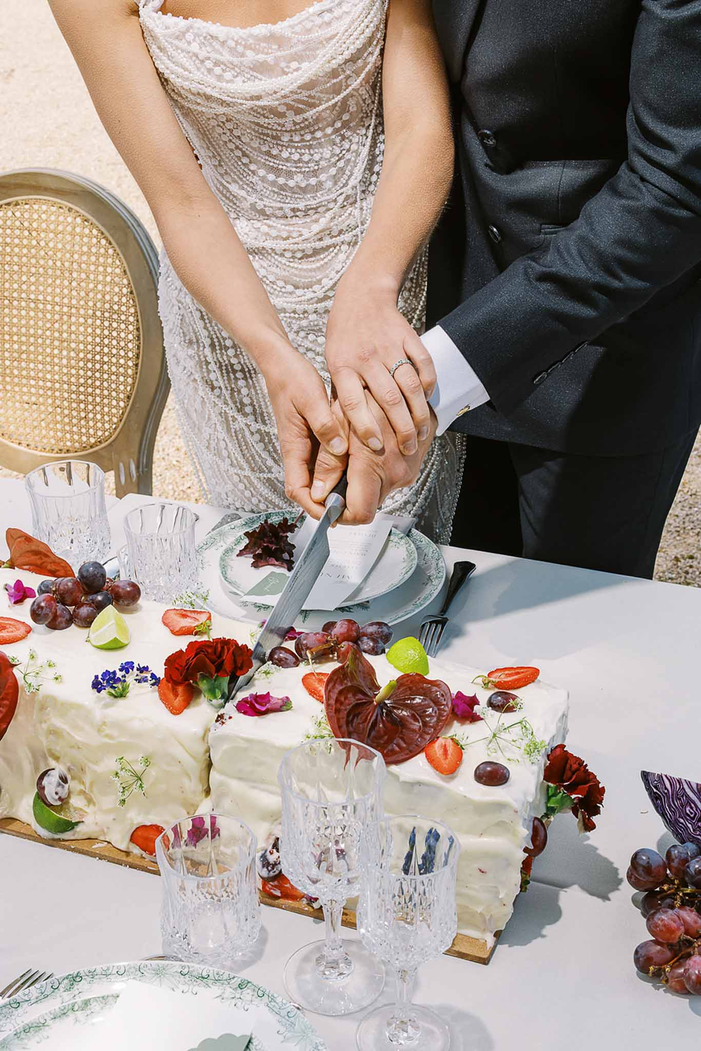 Bride and groom cutting white sheet cake decorated with strawberries grapes and dark red roses