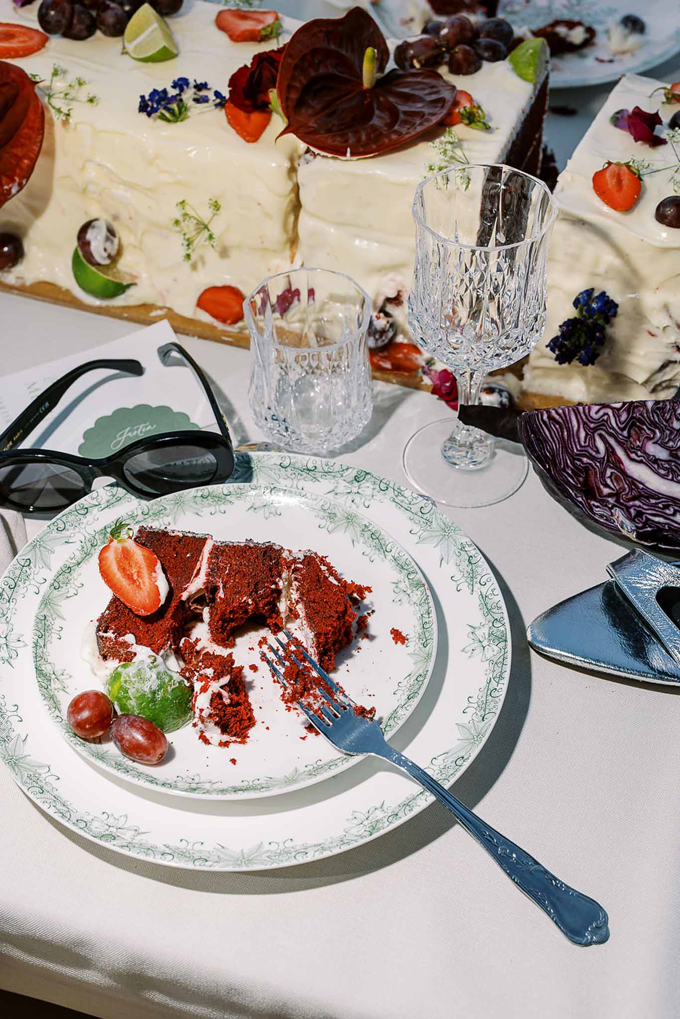 Red velvet cake slice and sheet cake decorated with burgundy anthuriums, berries, and citrus