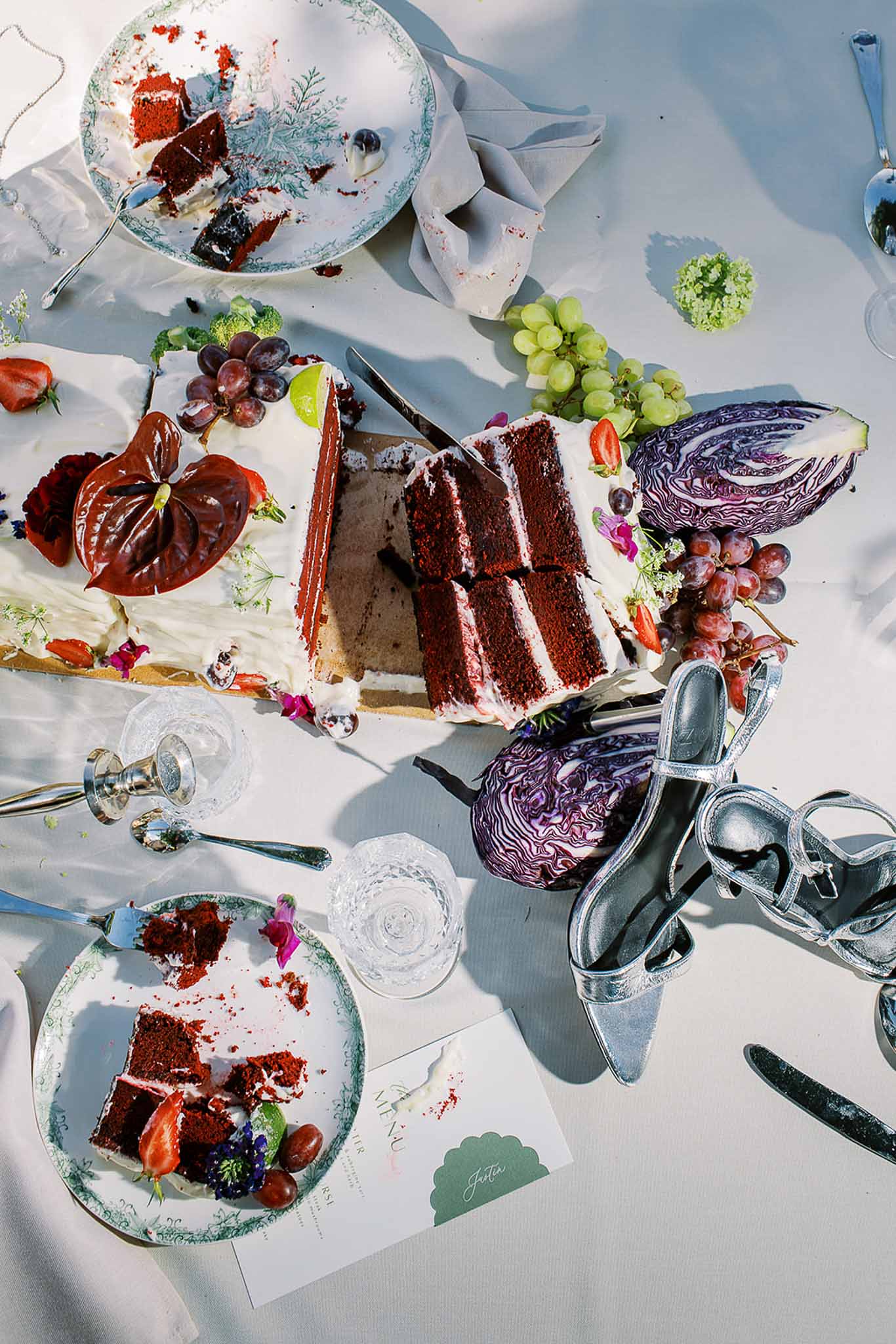 Overhead view of red velvet cake with anthurium strawberries and vintage botanical plates on white linen