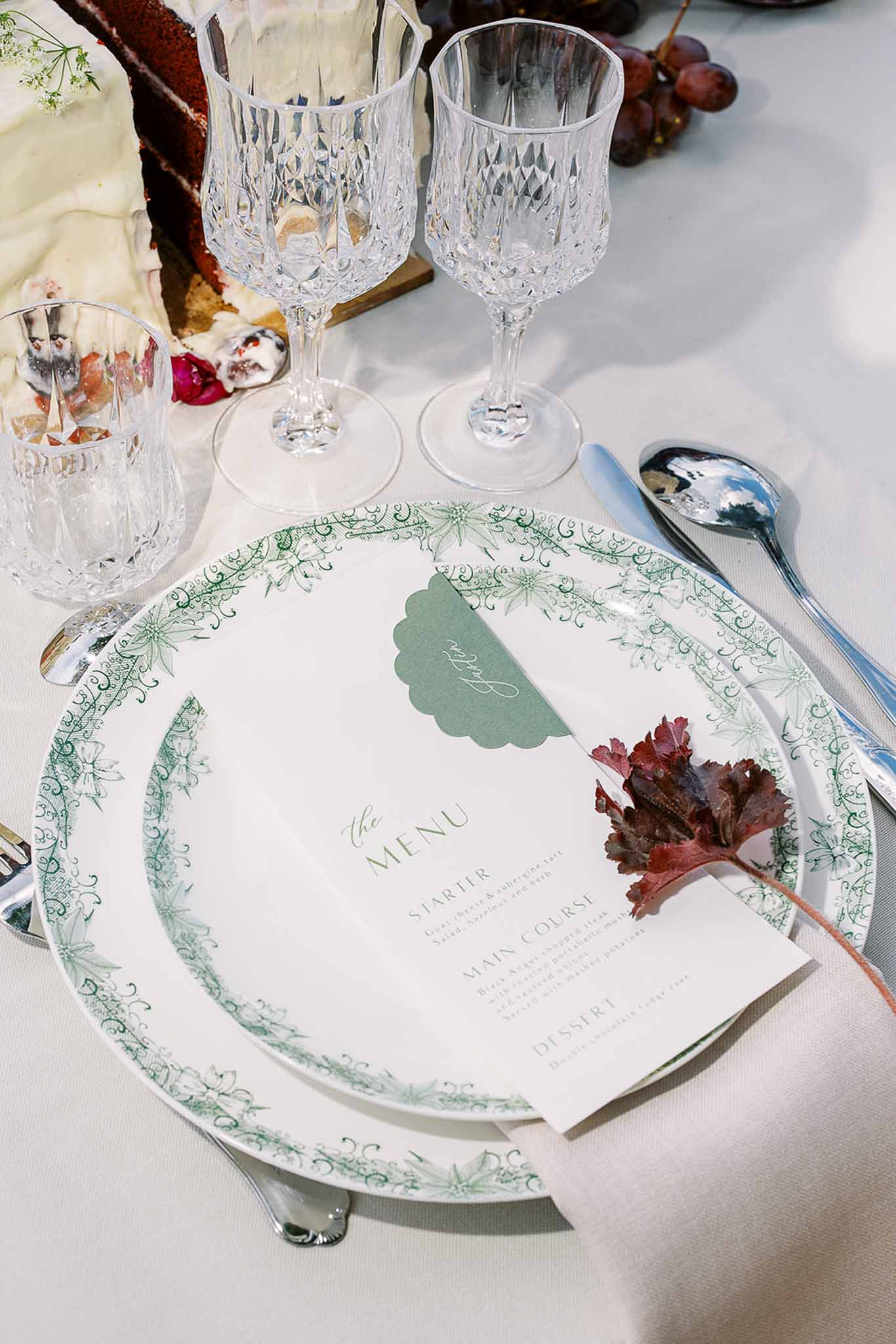 Reception place setting with botanical-print plate, menu card, crystal glasses, and burgundy leaf