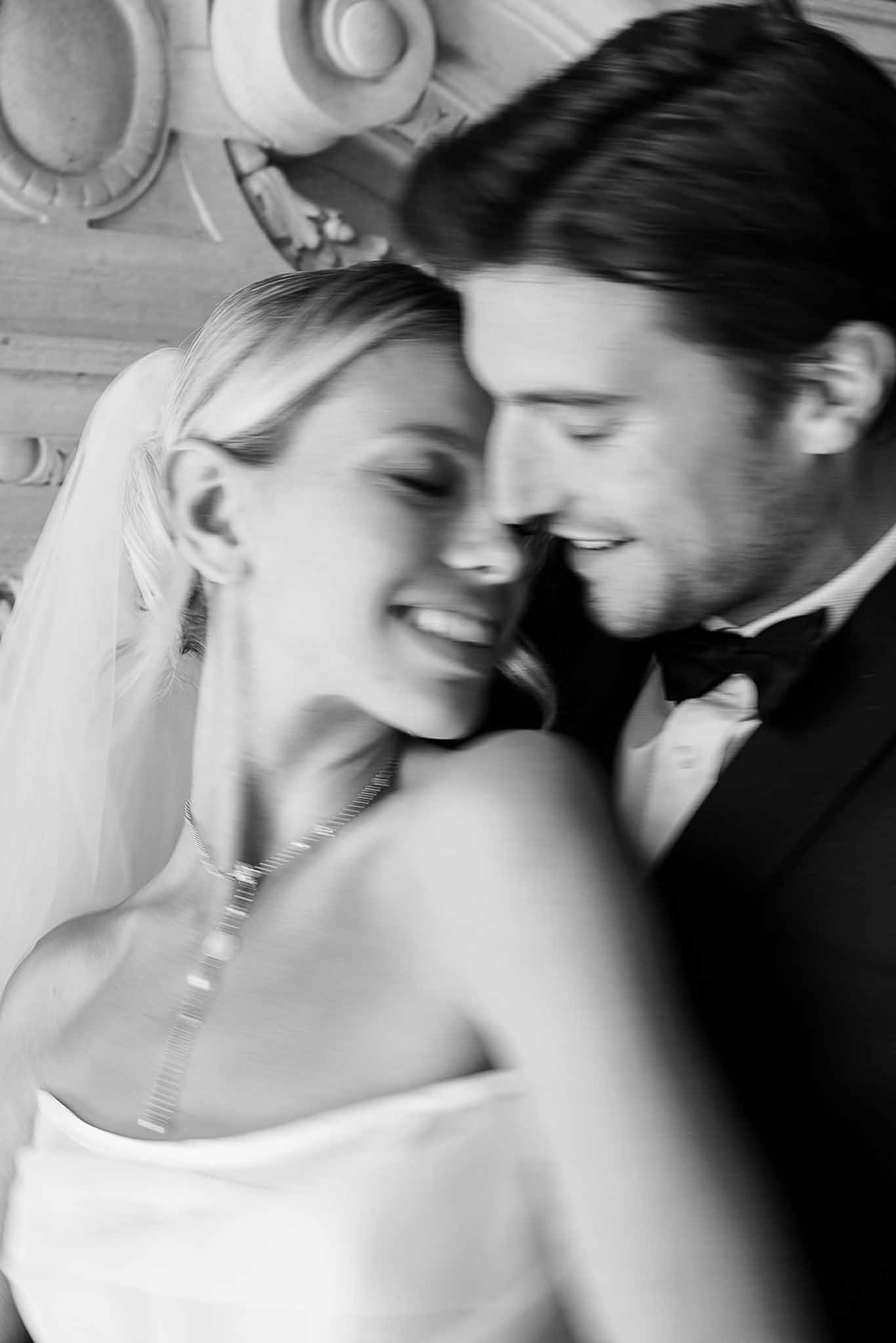 Black and white motion-blurred portrait of couple with foreheads touching in strapless gown and tuxedo with bow tie