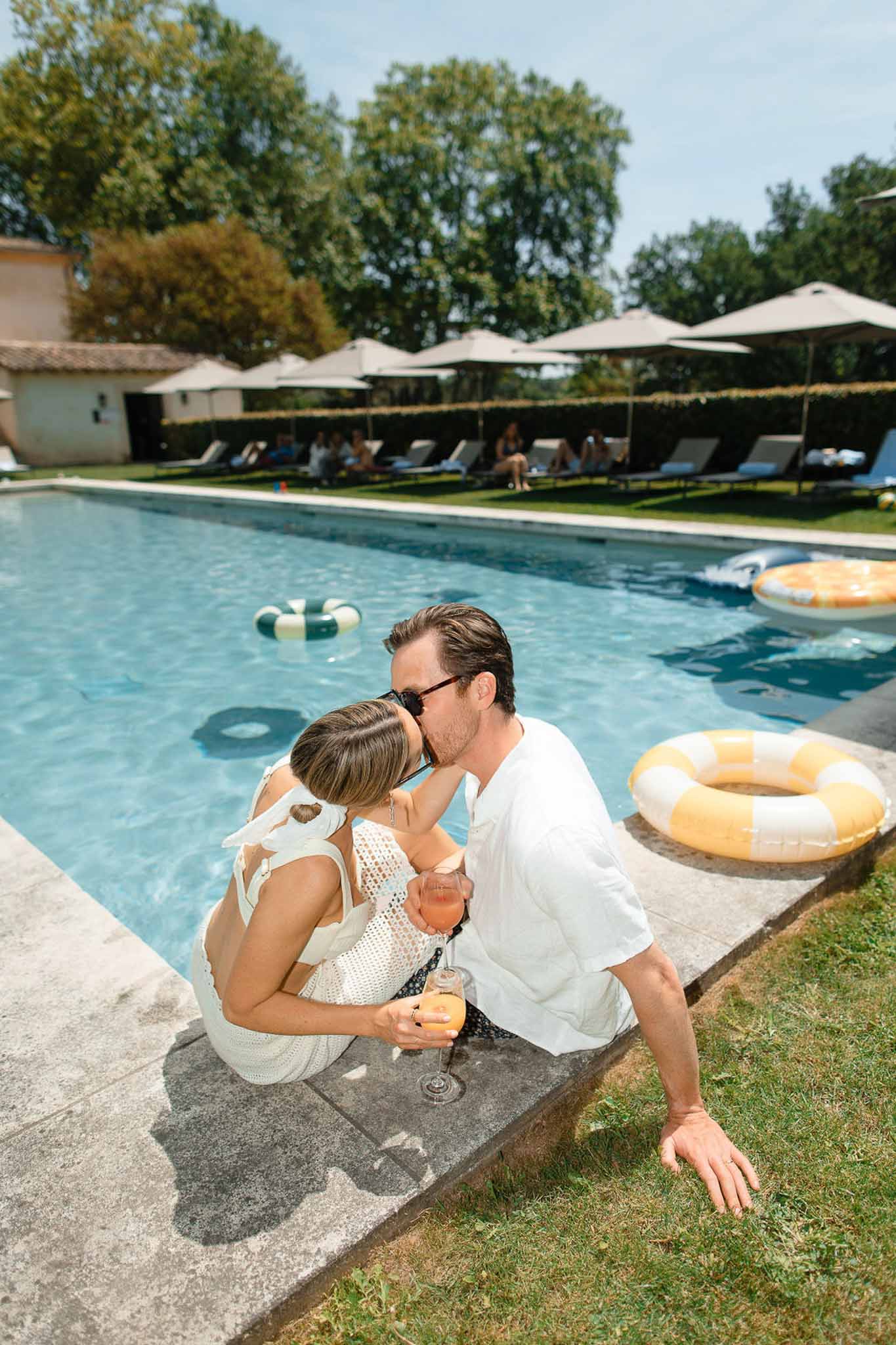 Groom kisses bride poolside with striped floats and guests on loungers at Provencal stone estate