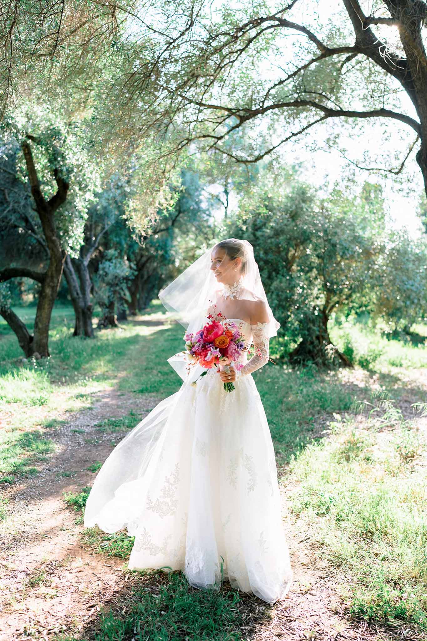 Bride in off-the-shoulder lace ball gown holding hot pink peony and orange rose bouquet in olive grove