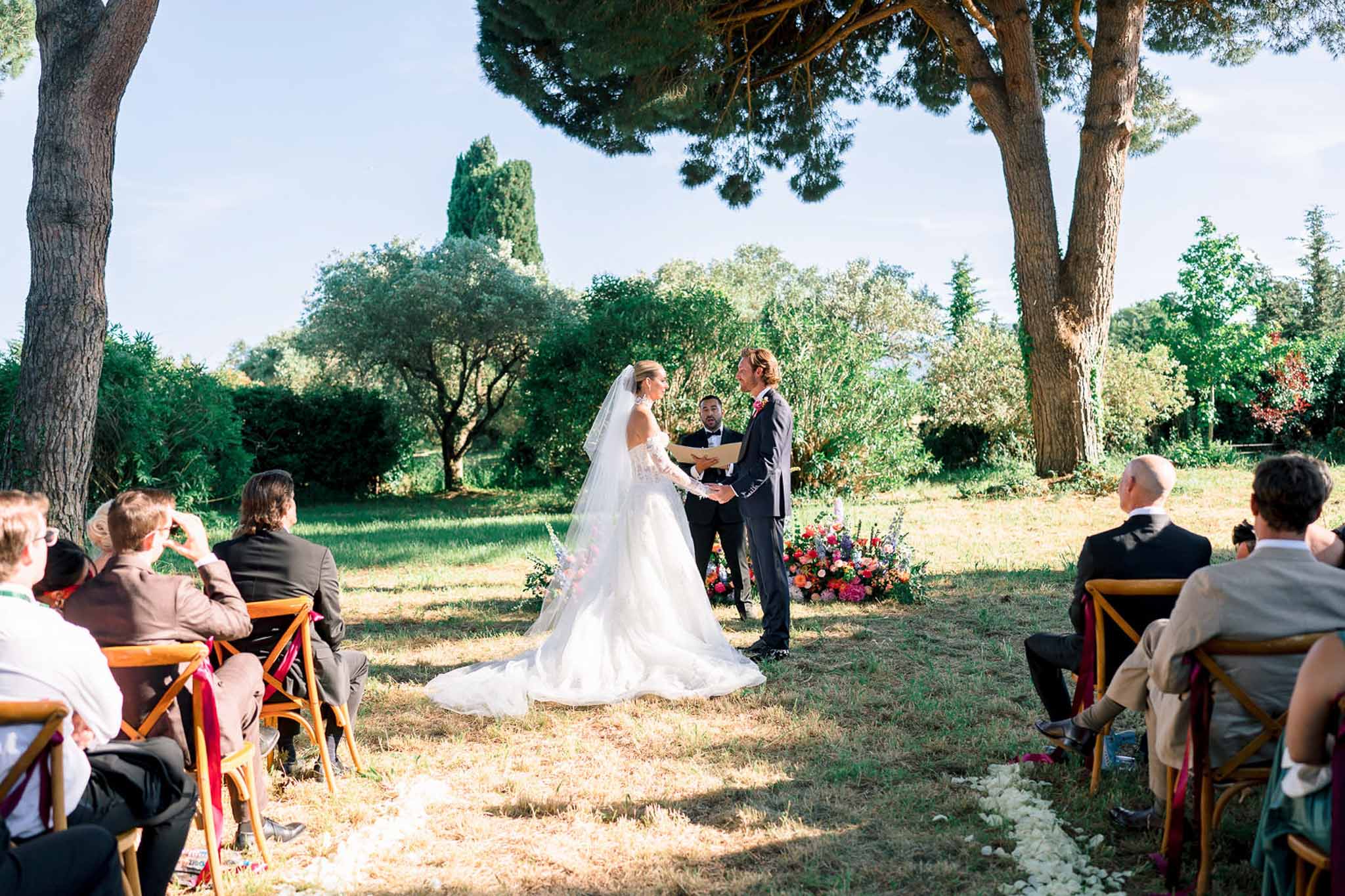 Bride in ballgown and groom in navy suit hold hands at garden altar with vibrant ground-level florals