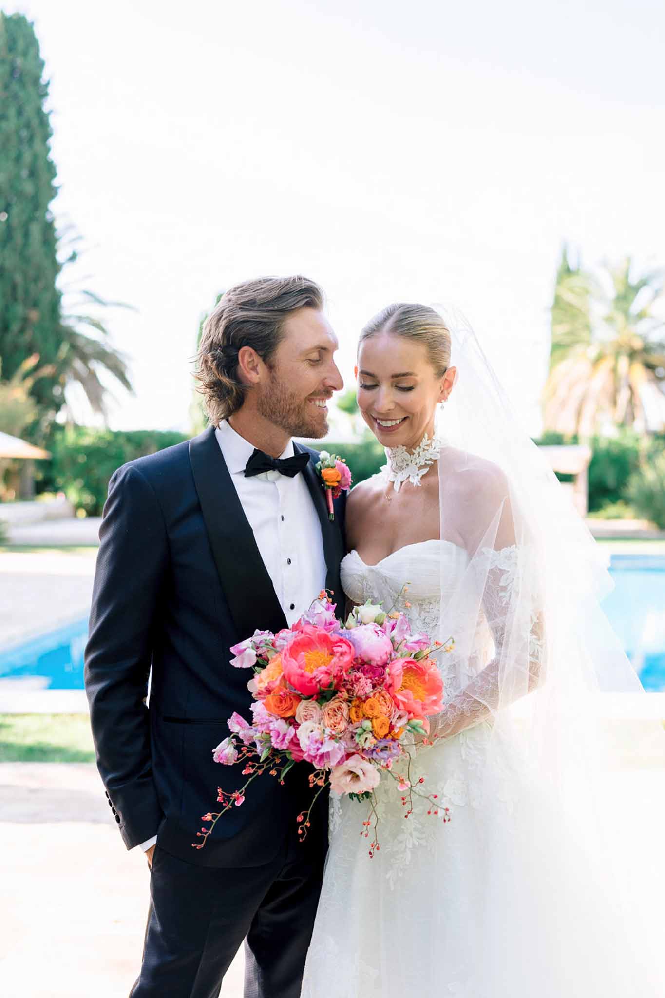 Bride and groom portrait beside a pool, bride holding cascading bouquet of pink peonies and coral roses