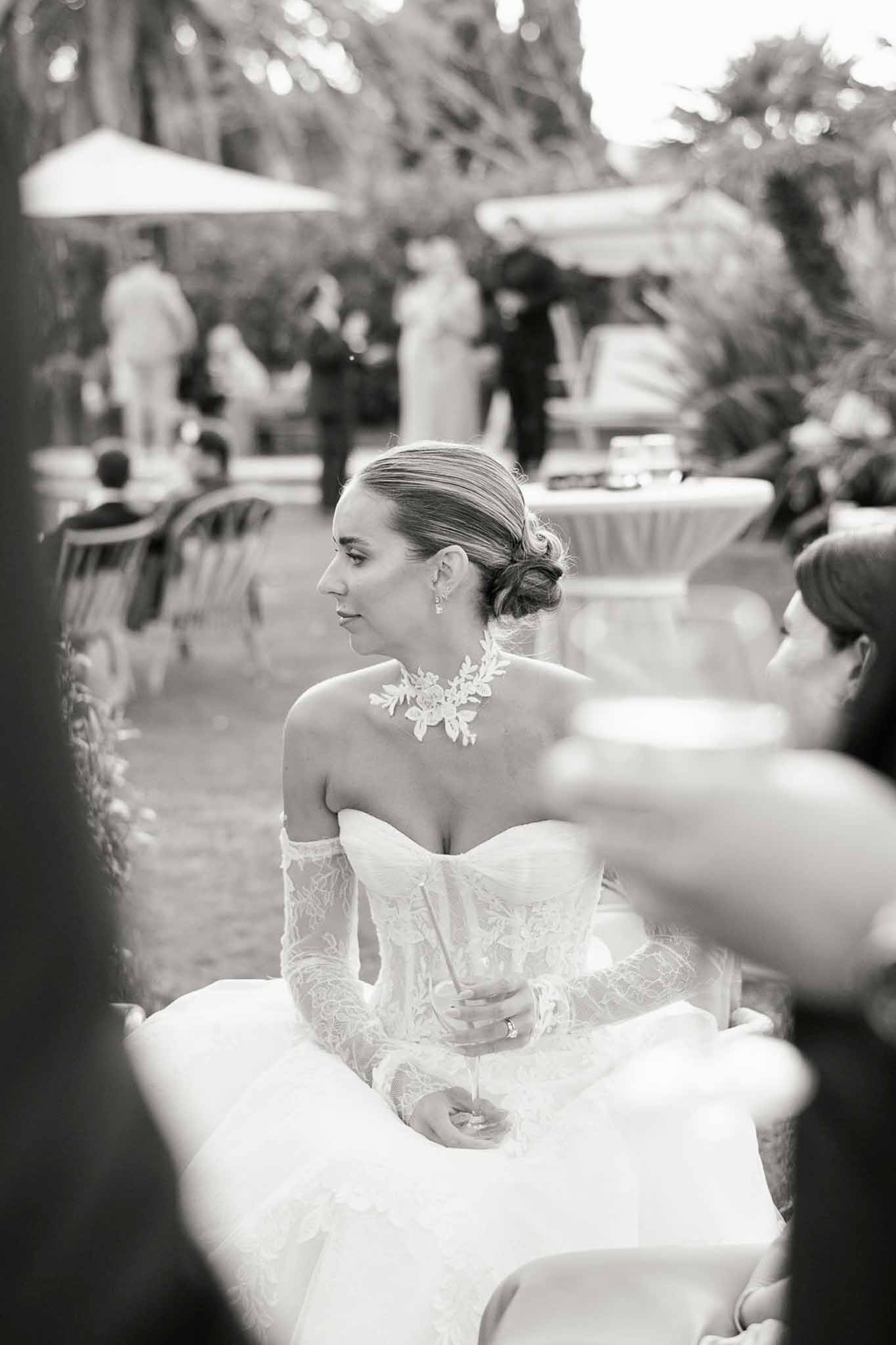 Black-and-white portrait of bride in strapless gown with lace gloves holding champagne during cocktail hour