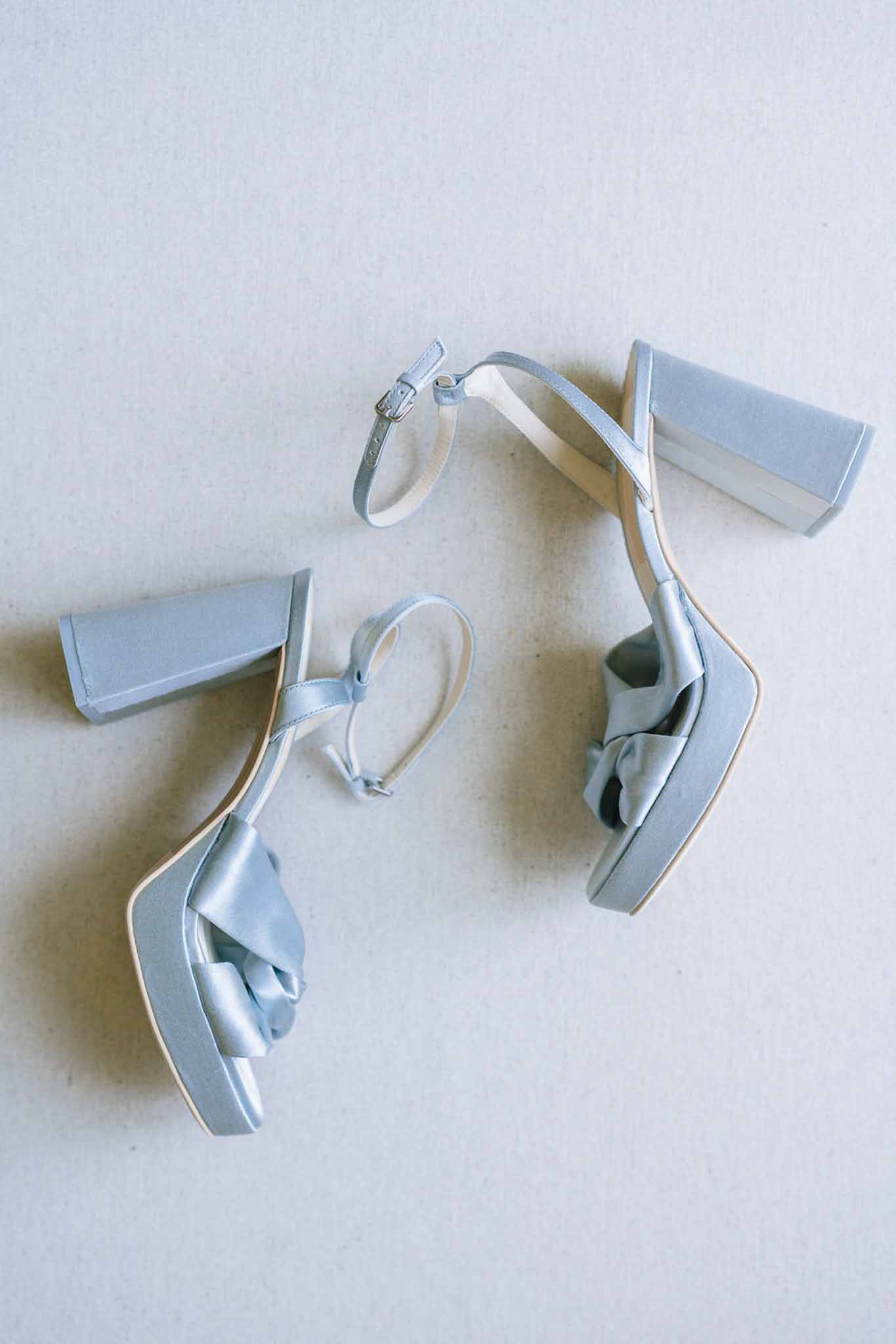 Powder blue satin bridal heels with block heel, ankle strap, and twisted knot detail on grey surface