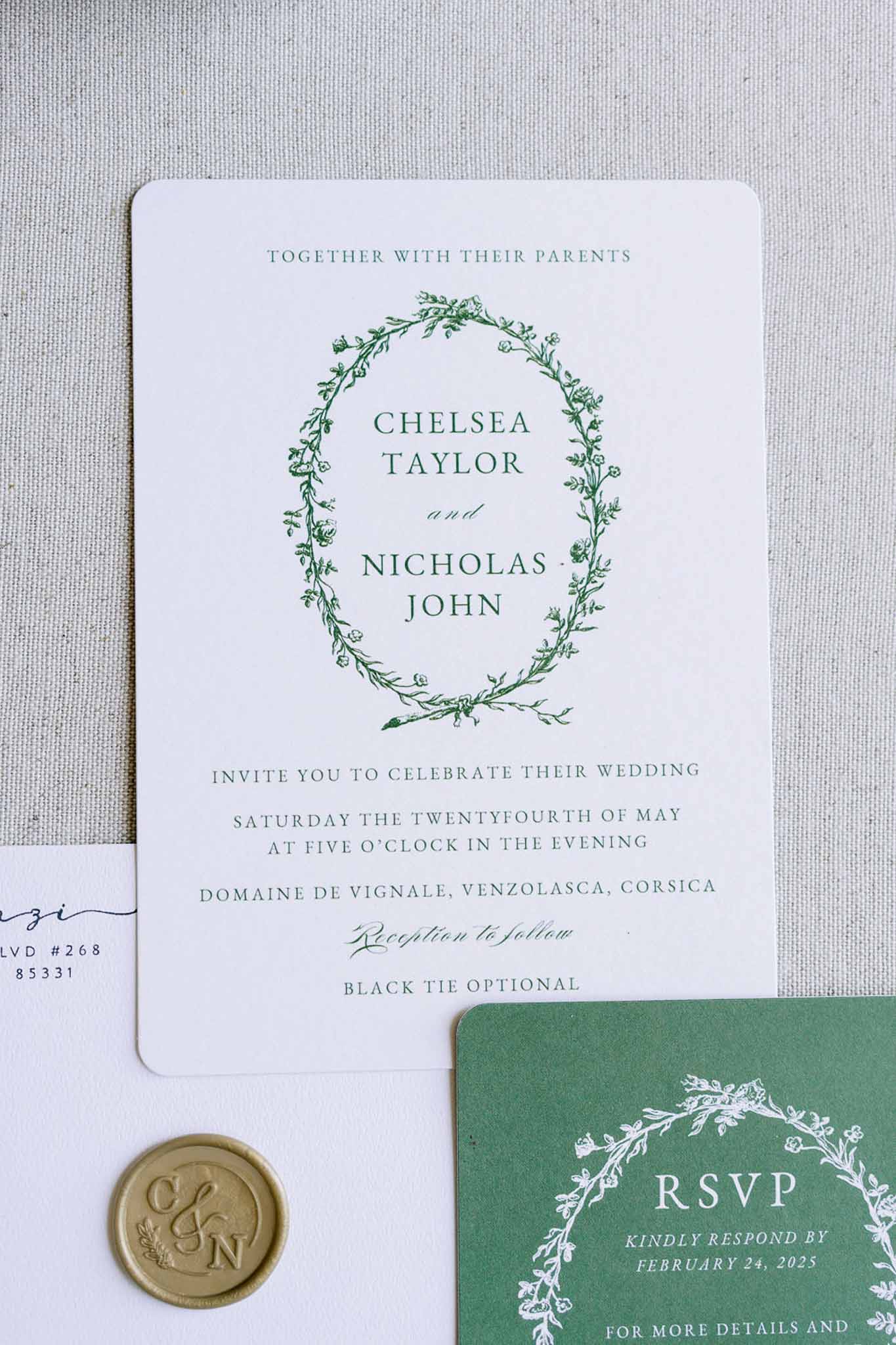 Forest green botanical stationery suite with wreath illustration and gold wax seal on linen surface