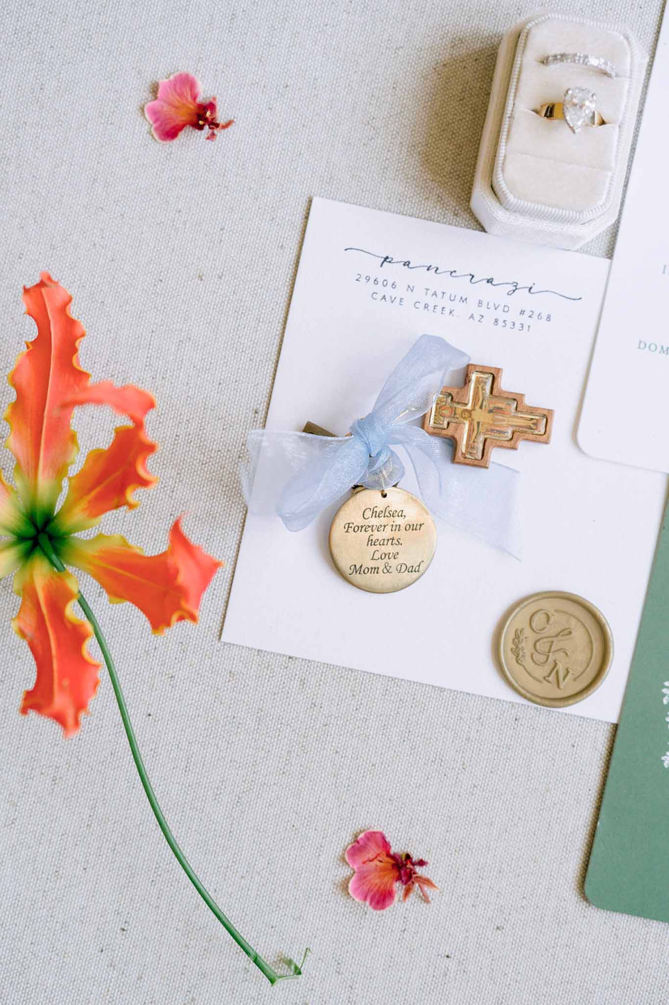 Flat lay with calligraphy envelope gold wax seal terracotta cross velvet ring box and tropical flowers