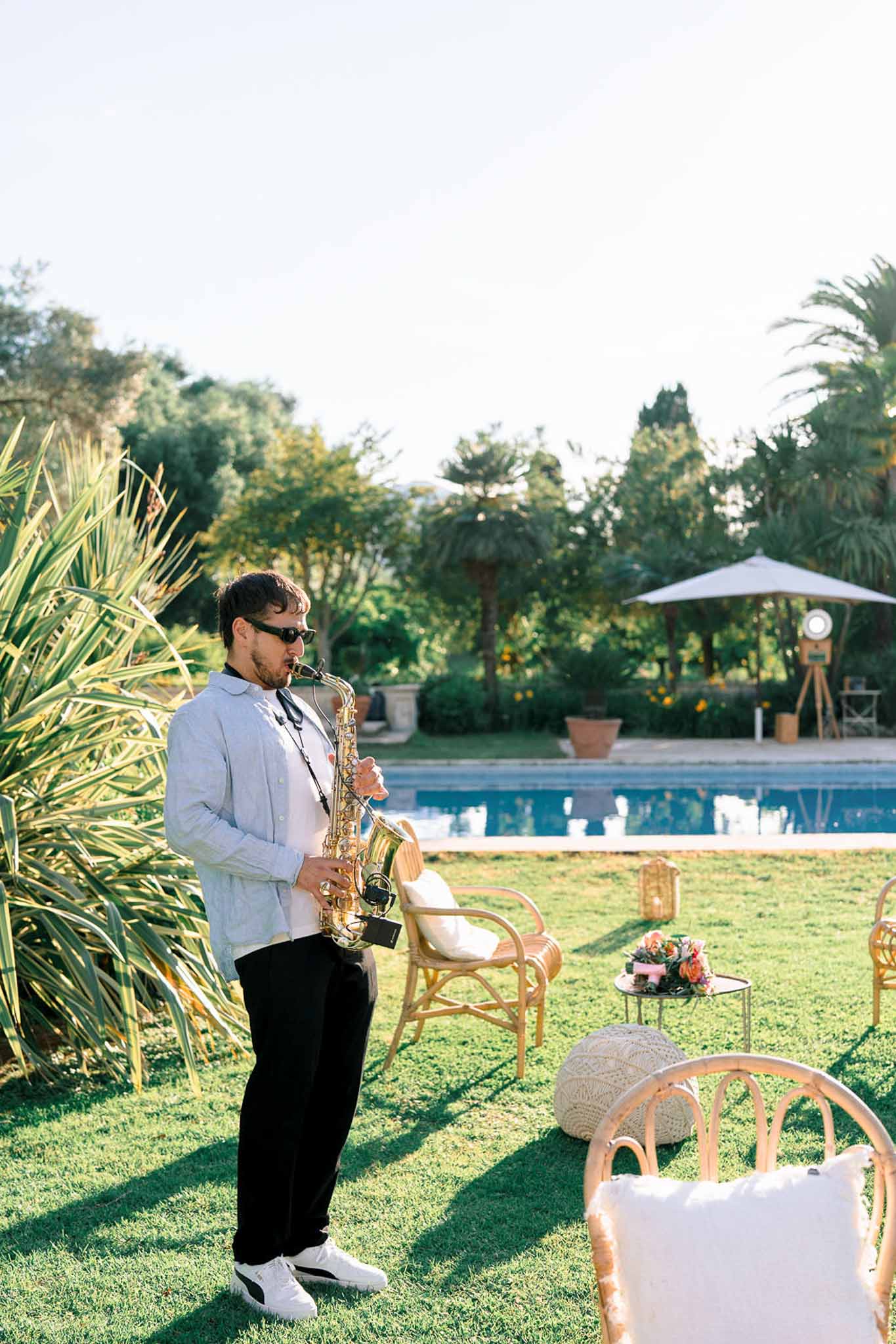 Saxophonist playing beside a swimming pool with rattan lounge seating and coral and peach flower arrangement