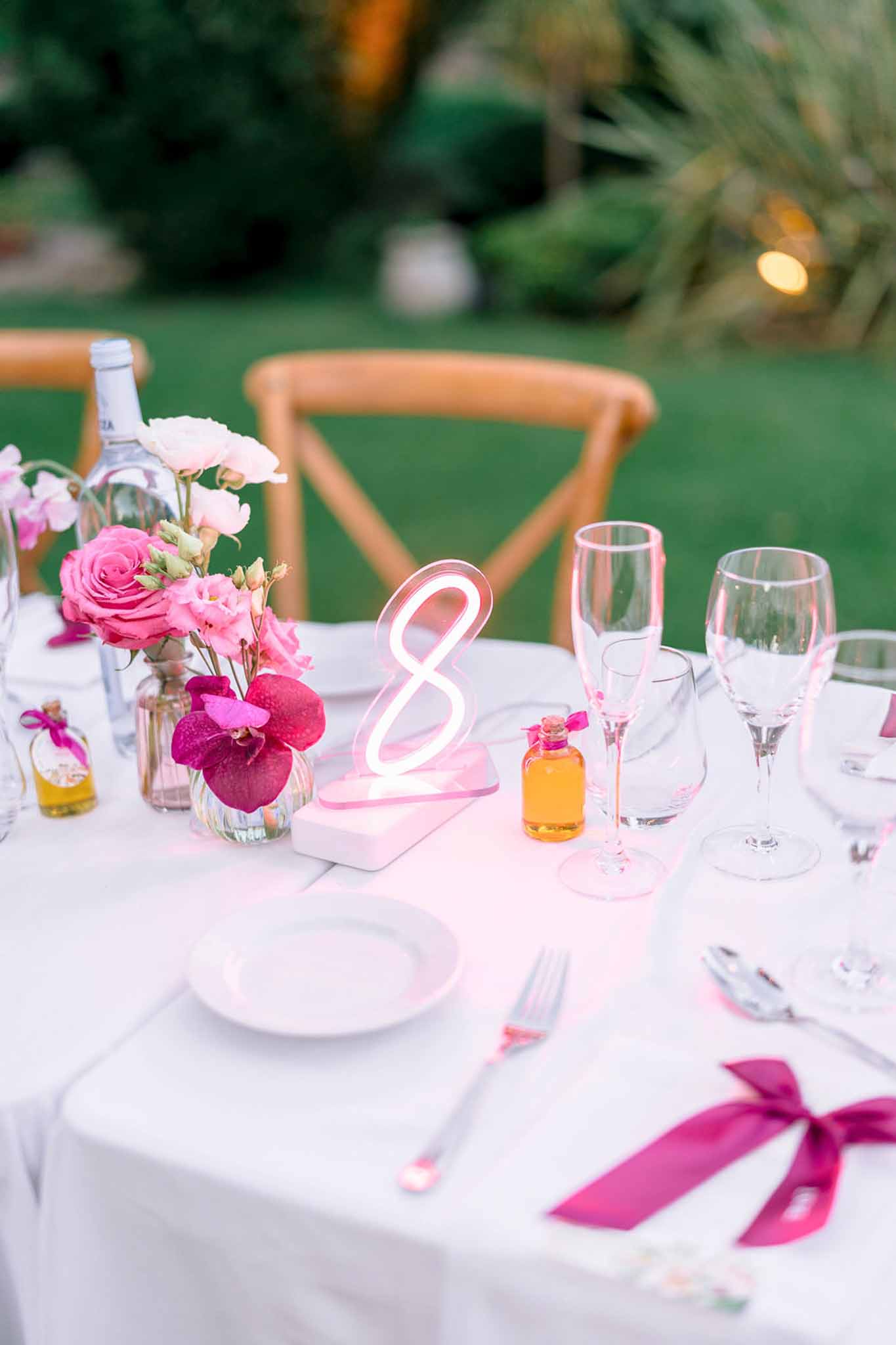 Reception table with hot pink roses, neon number eight, fuchsia ribbon napkins, and champagne flutes