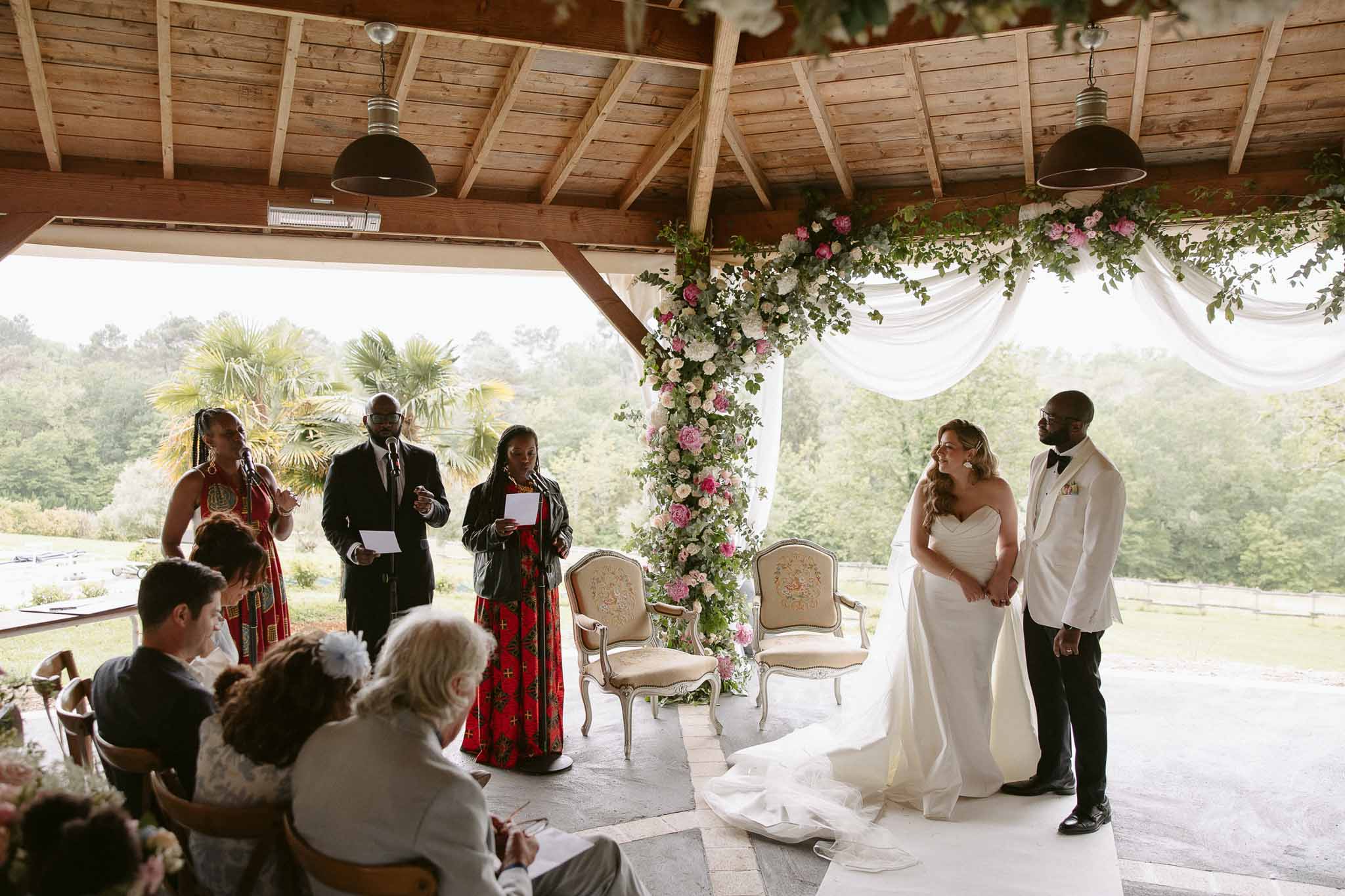 Ceremony under wooden pavilion with hot pink and blush rose floral column, bride and groom facing officiants