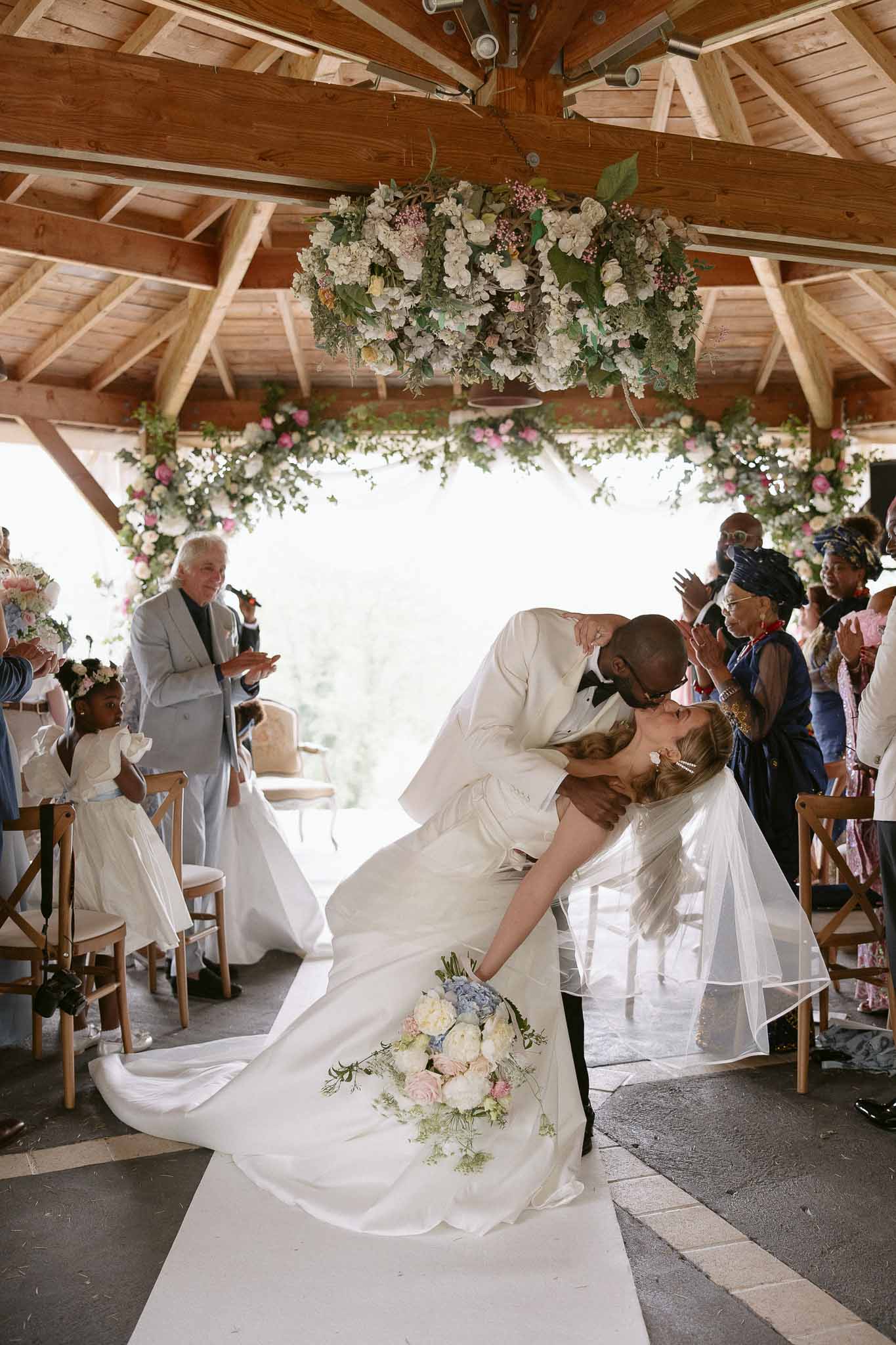 Groom dips bride for a kiss at end of ceremony aisle beneath hanging floral installation