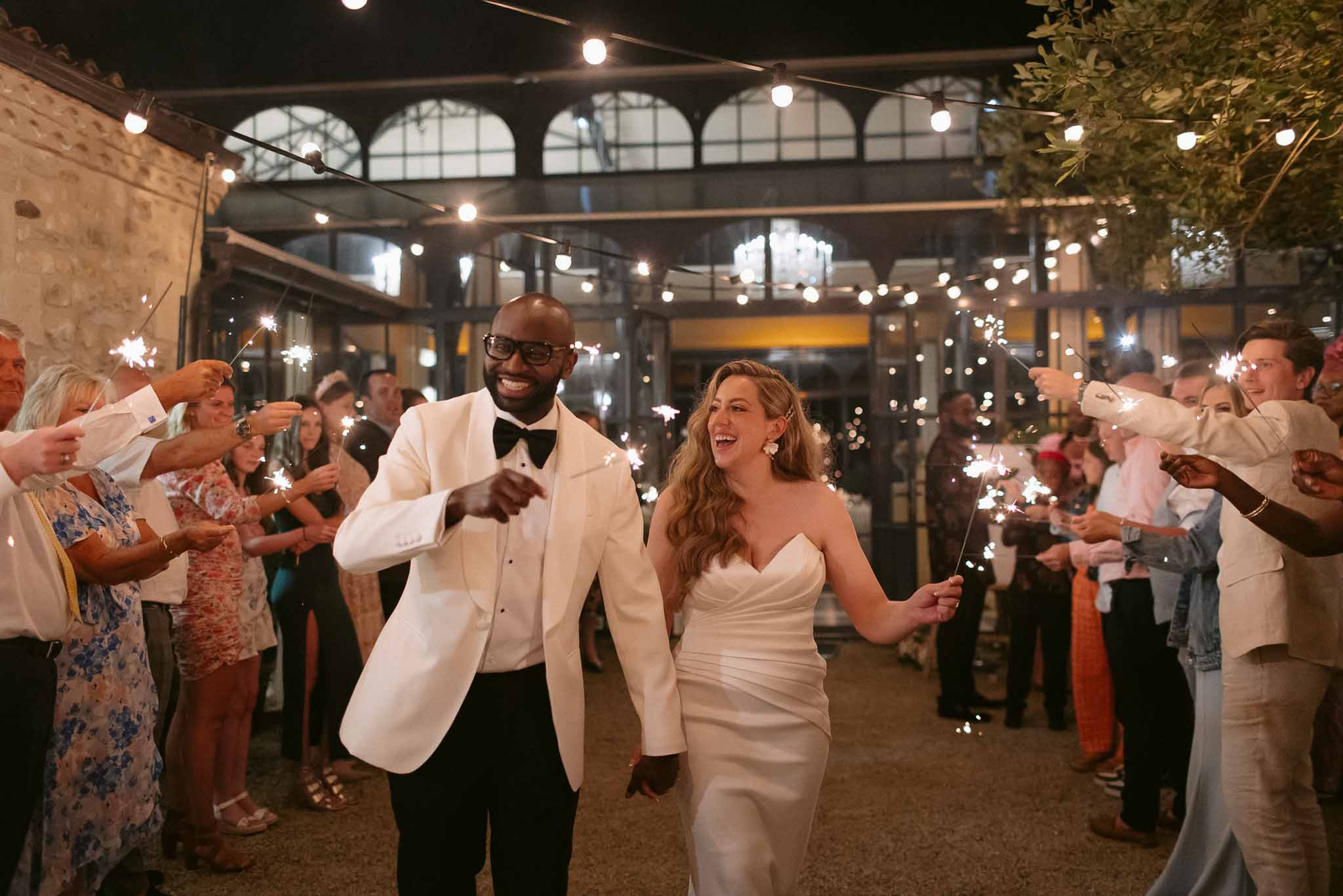 Couple with sparklers walking through guest tunnel outside industrial-style venue at night
