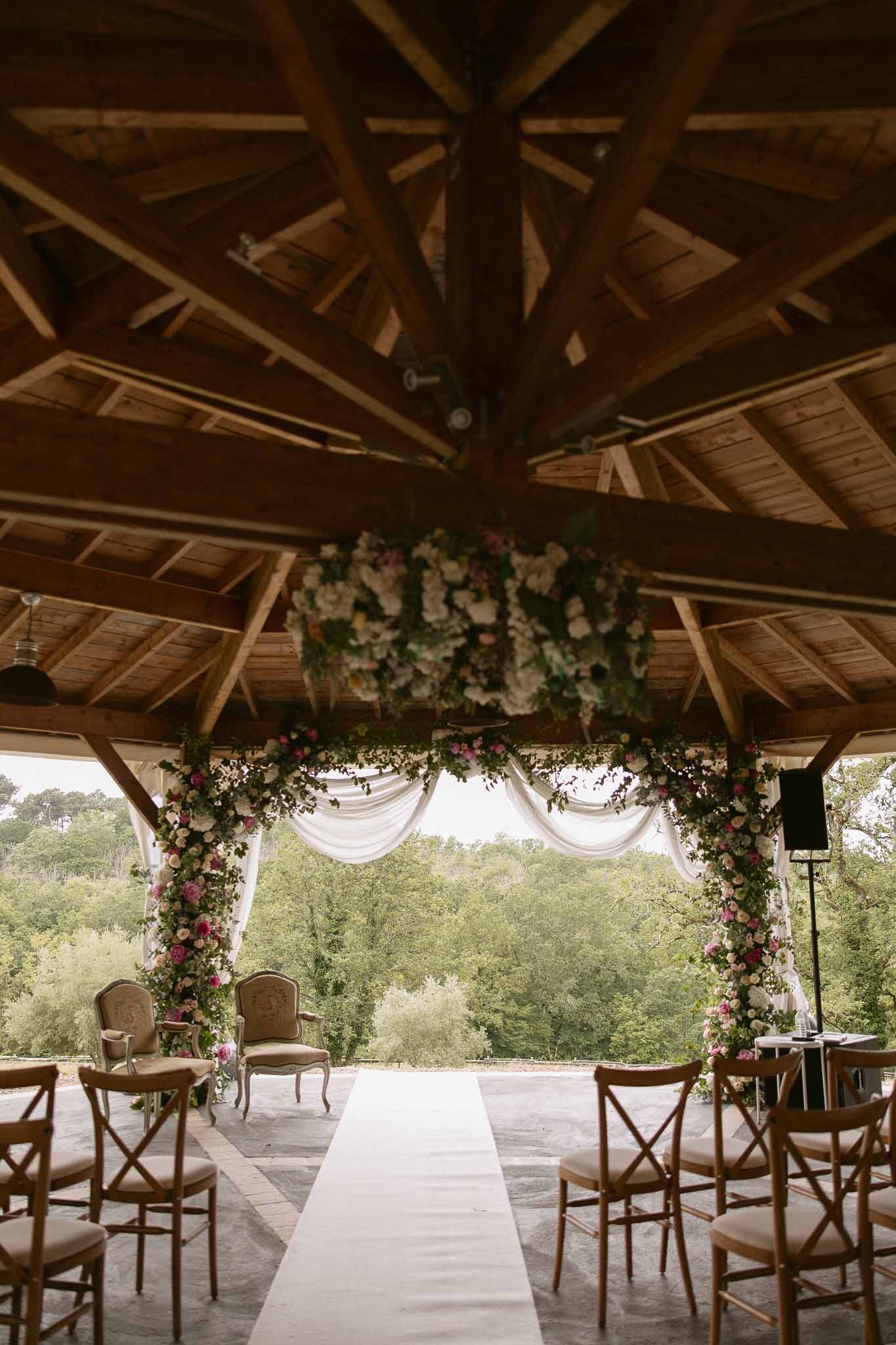 Open-air pavilion ceremony setup with pink and white rose arch and suspended floral installation