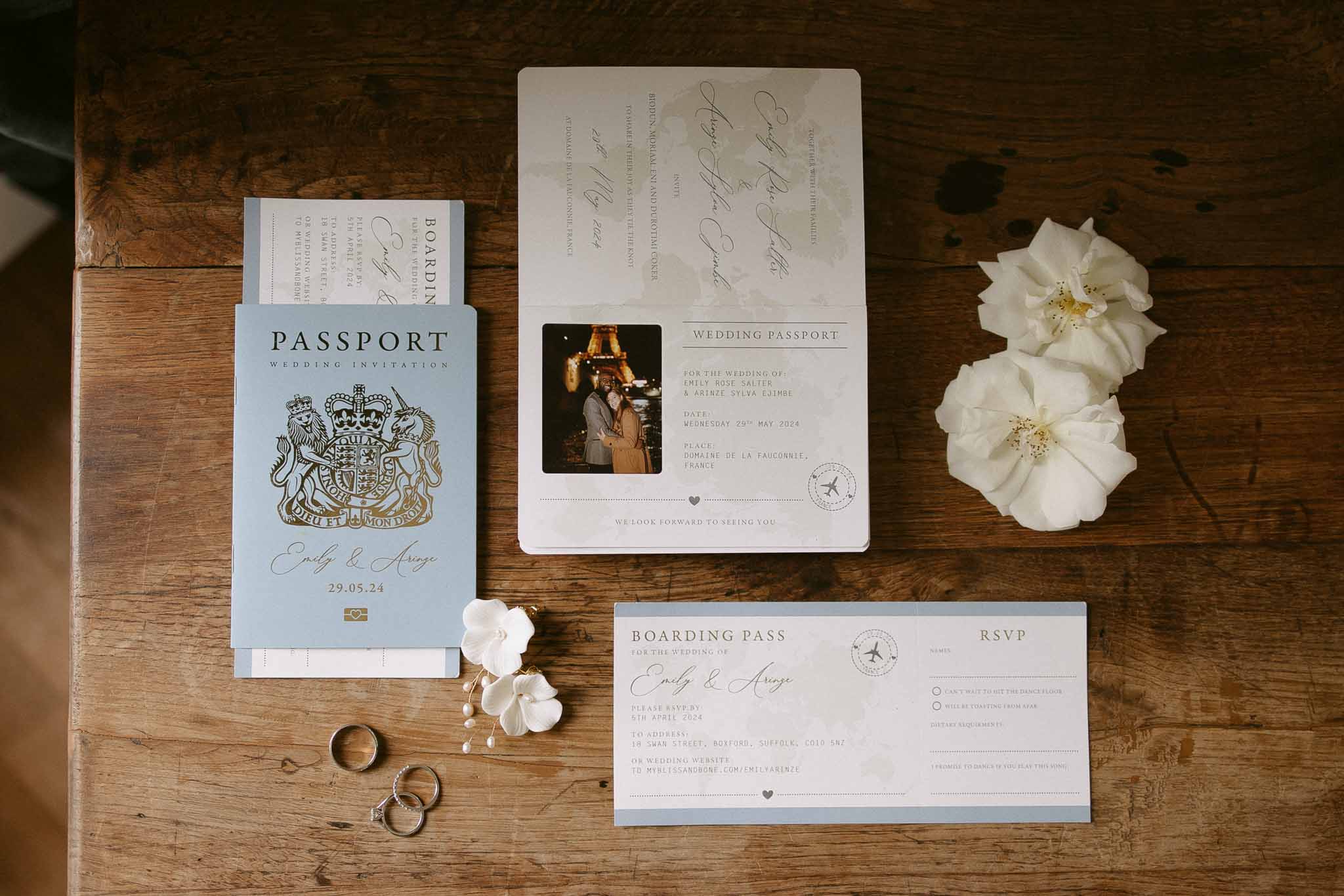 Passport-style blue invitation with boarding pass RSVP, gold rings, and pearl orchid earrings on wood