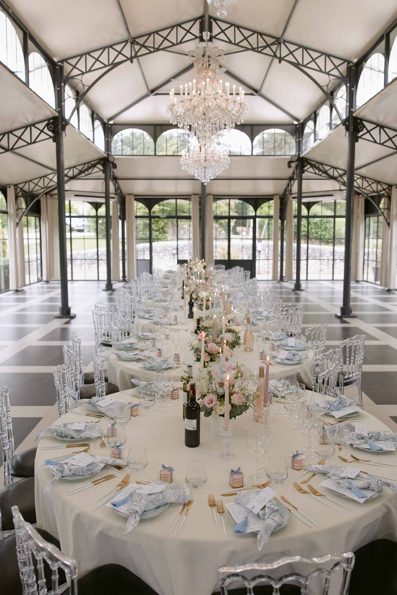 Glass conservatory reception with blush florals, blue toile napkins, and crystal chandelier on checkered floor