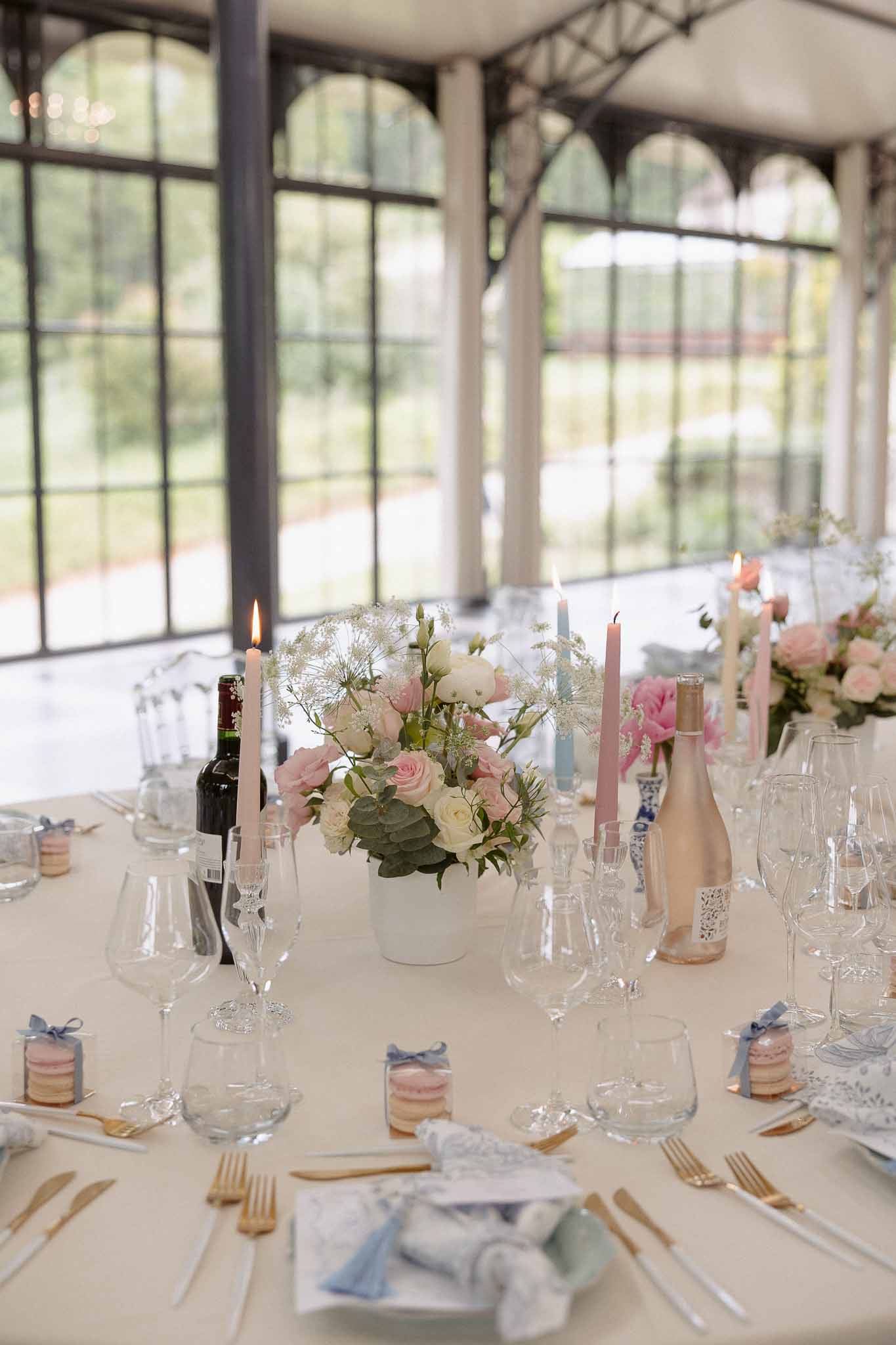 Reception table with blush roses and dusty blue napkins, macaron favors, and gold flatware in orangery