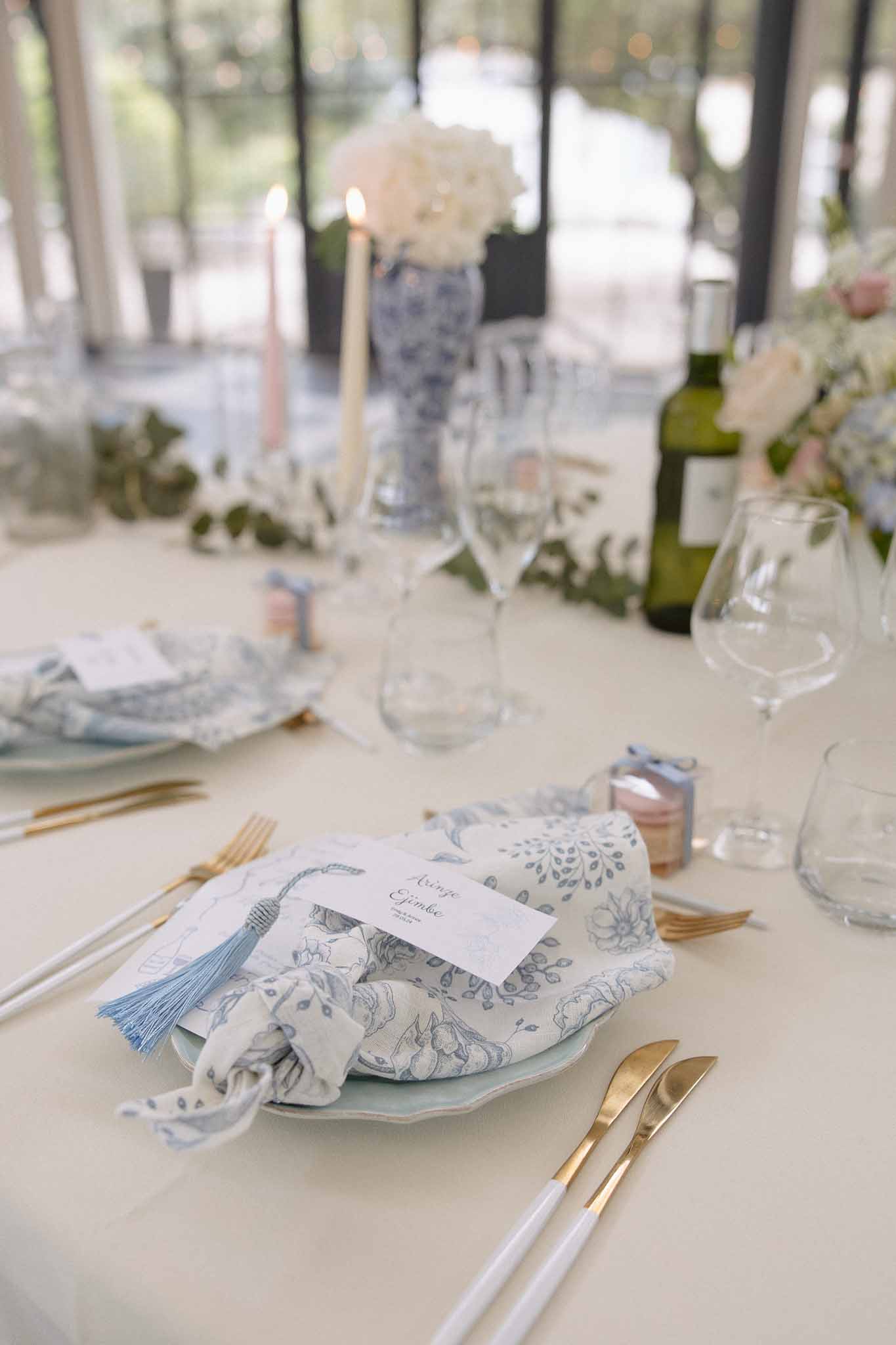 Blue toile napkin on pale blue plate with gold flatware, hydrangea bud vases, and eucalyptus runner