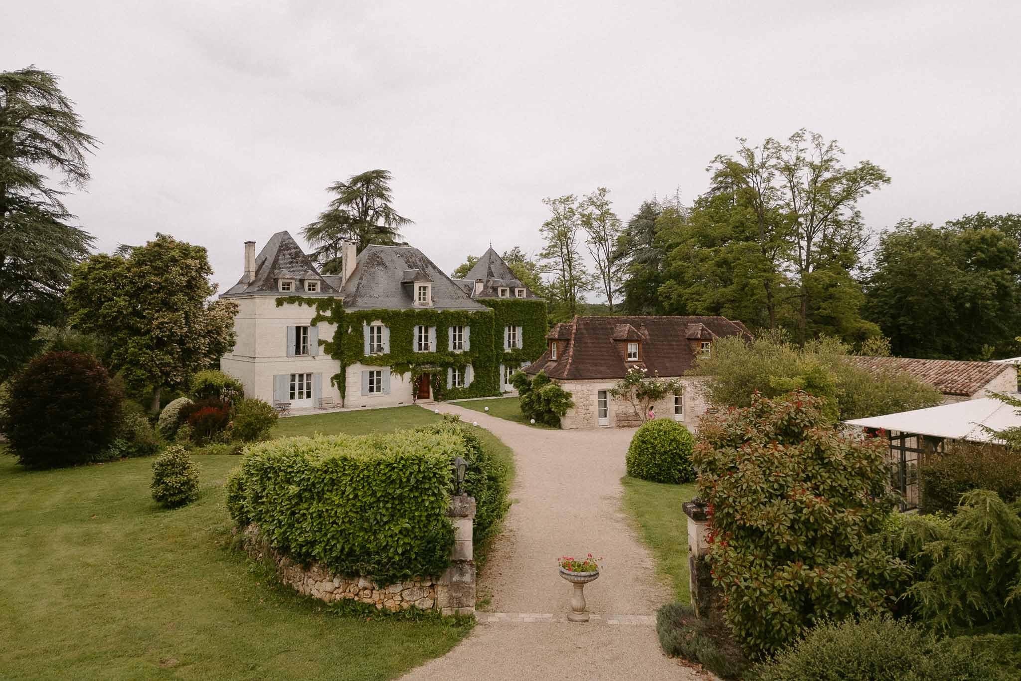 Ivy-covered chateau with slate turrets, blue shutters, glass canopy, and stone pillar entrance on gravel driveway