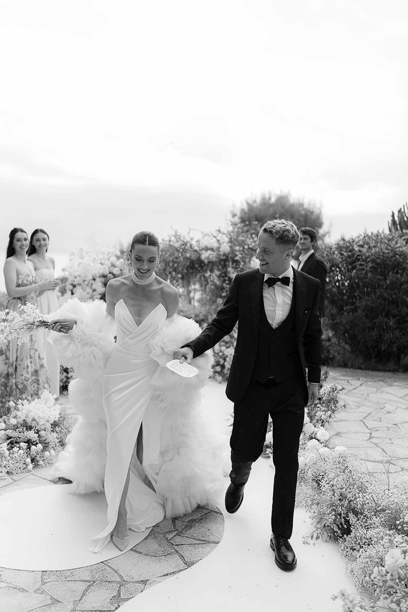 Black and white photo of bride and groom walking down the aisle after ceremony, holding hands and smiling
