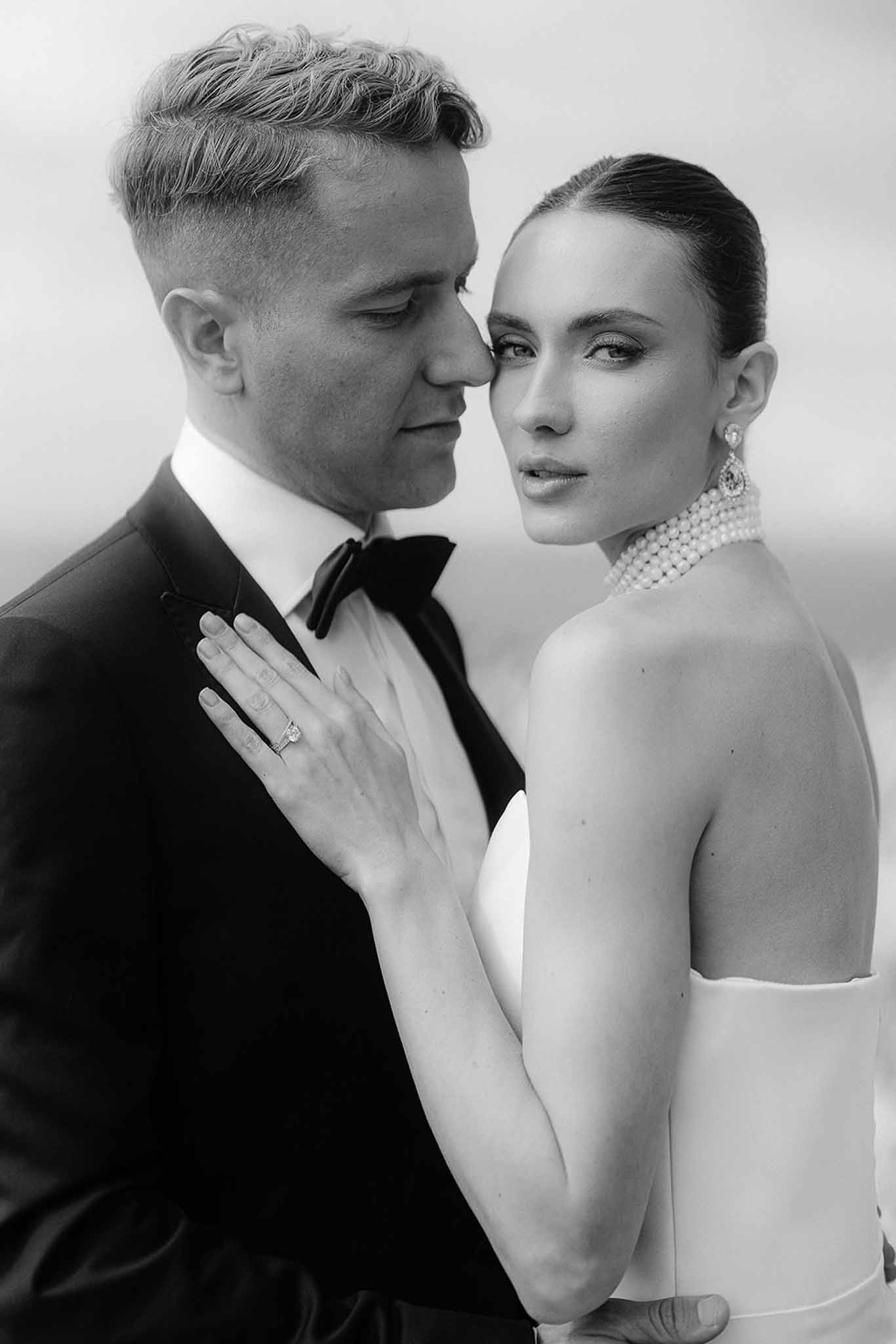 Black and white close-up of couple with bride's pearl choker and diamond ring on groom's chest