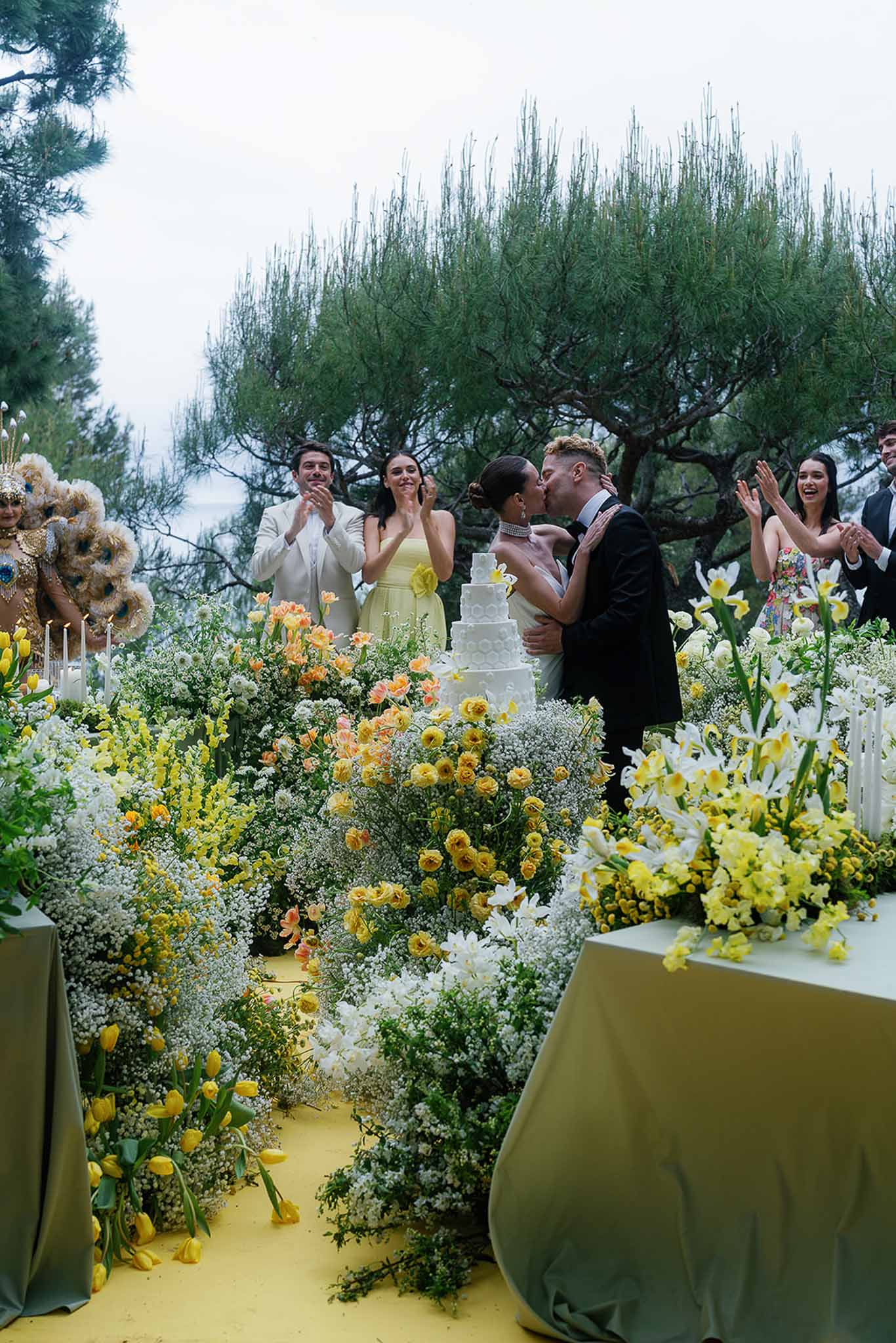 Couple kissing at cake cutting surrounded by yellow tulips and garden roses on yellow carpet