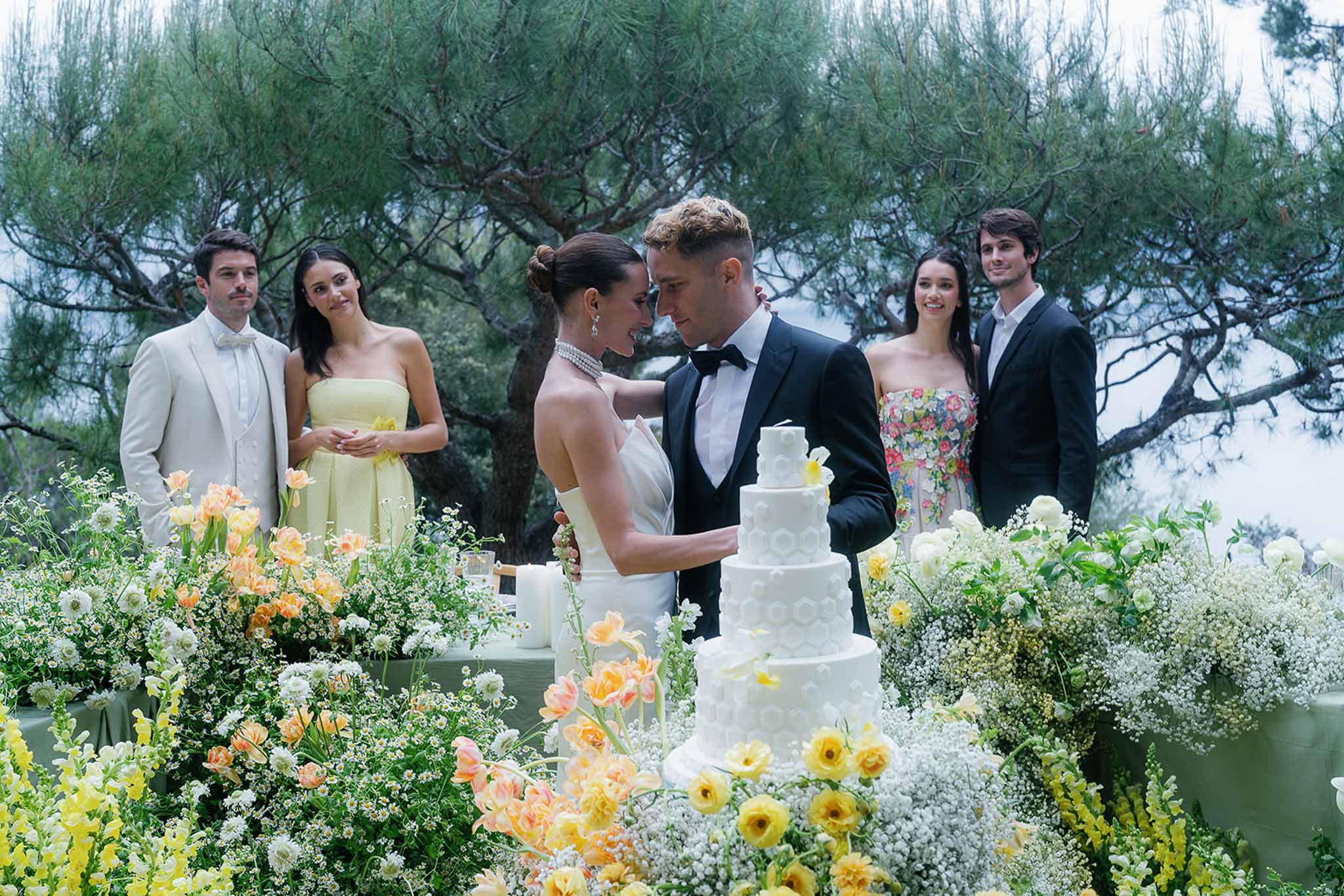 Couple and bridal party at five-tier cake with yellow ranunculus and peach tulip garden display