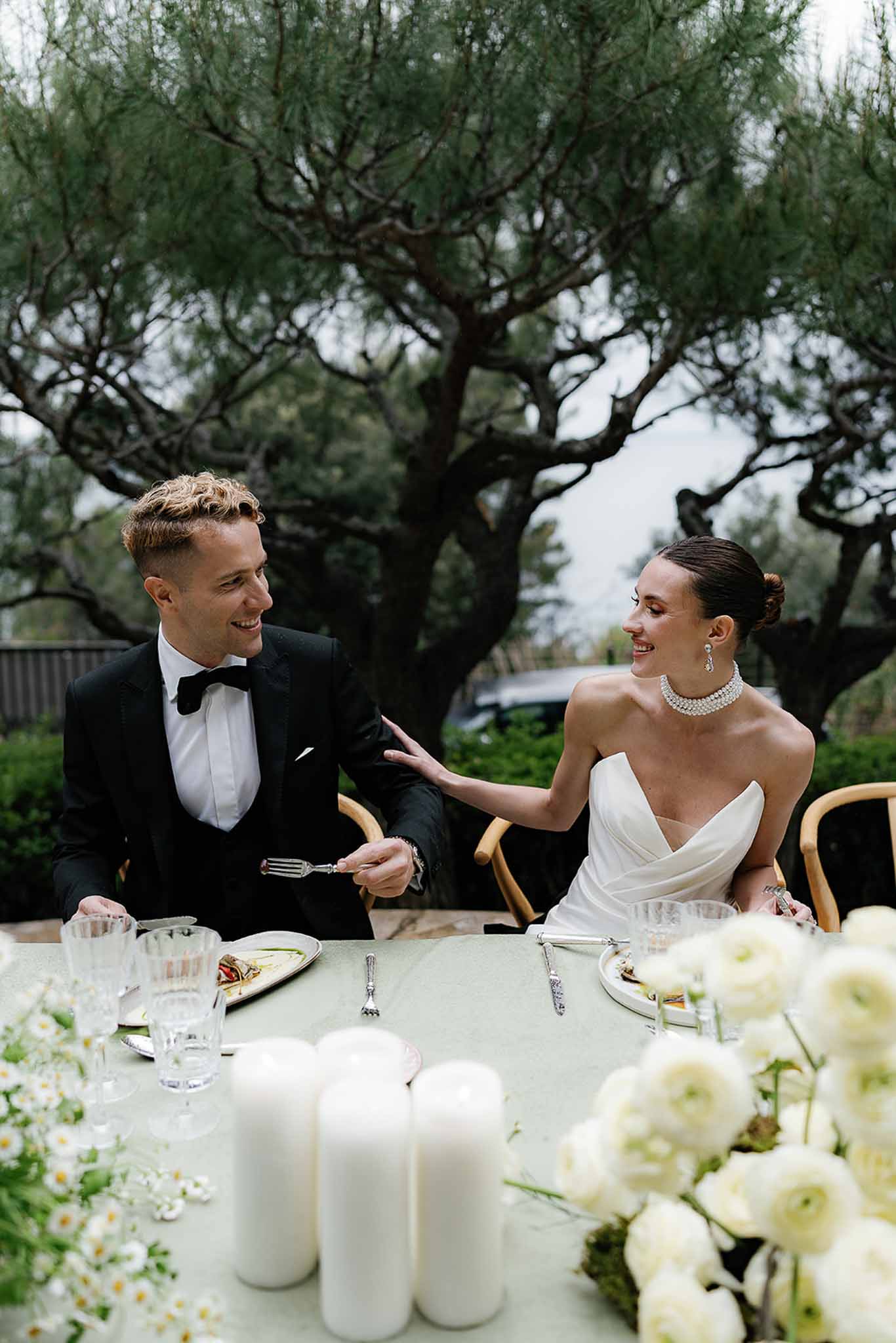 Bride and groom laughing at sweetheart table with white ranunculus centerpiece and pillar candles