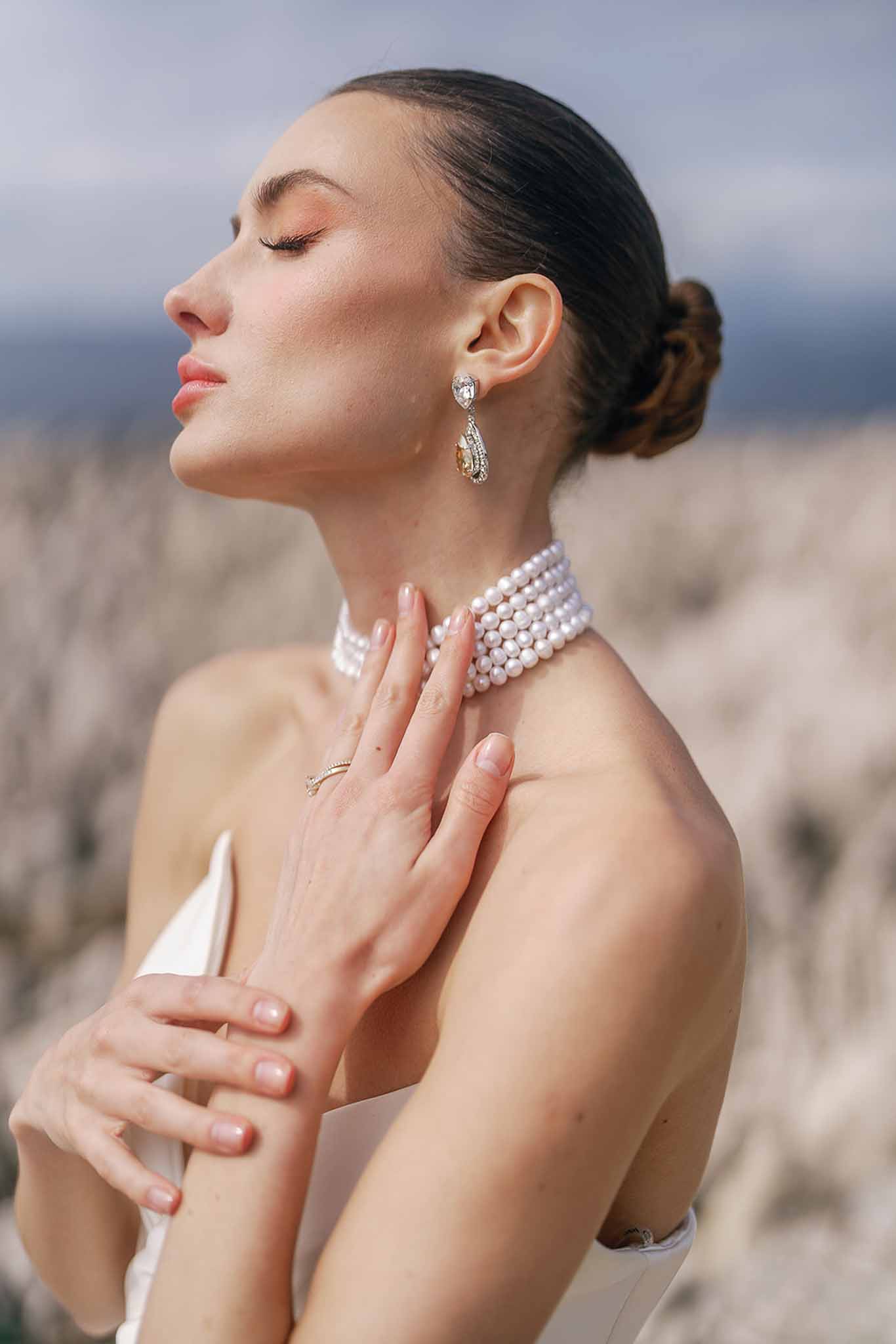 Bride in profile with eyes closed wearing pearl choker necklace, crystal earrings, and sleek updo