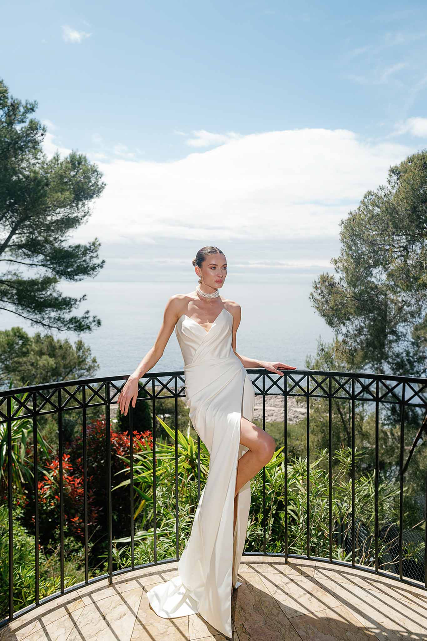 Bride in ivory satin column dress with pearl choker posing on terrace overlooking the sea at Cap Ferrat