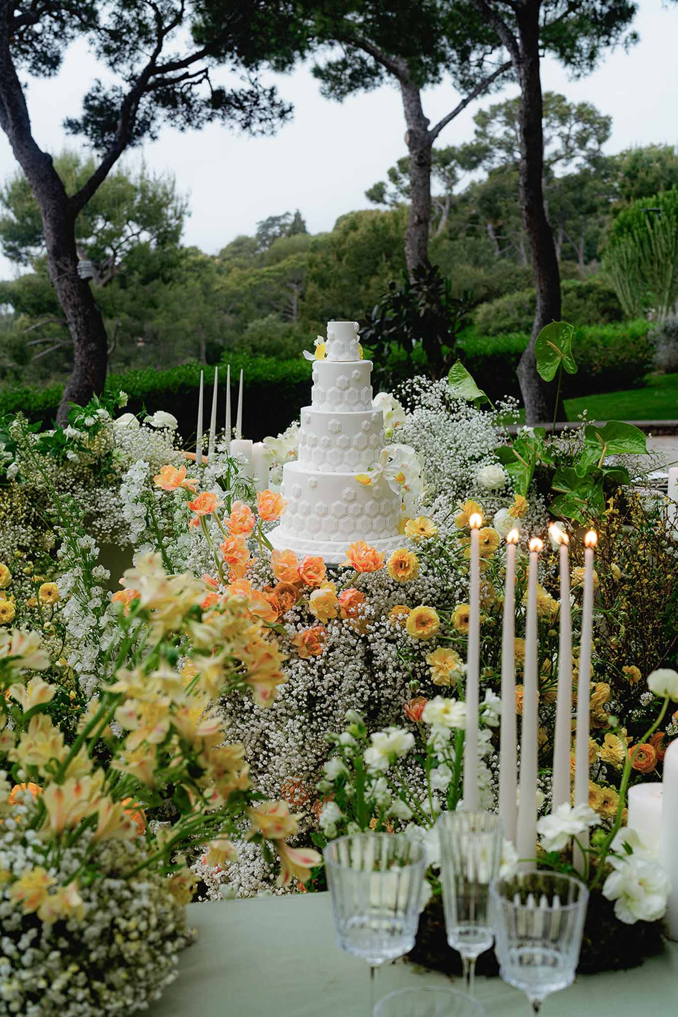 Five-tier honeycomb-textured white cake with orange tulips yellow ranunculus orchids and blush taper candles