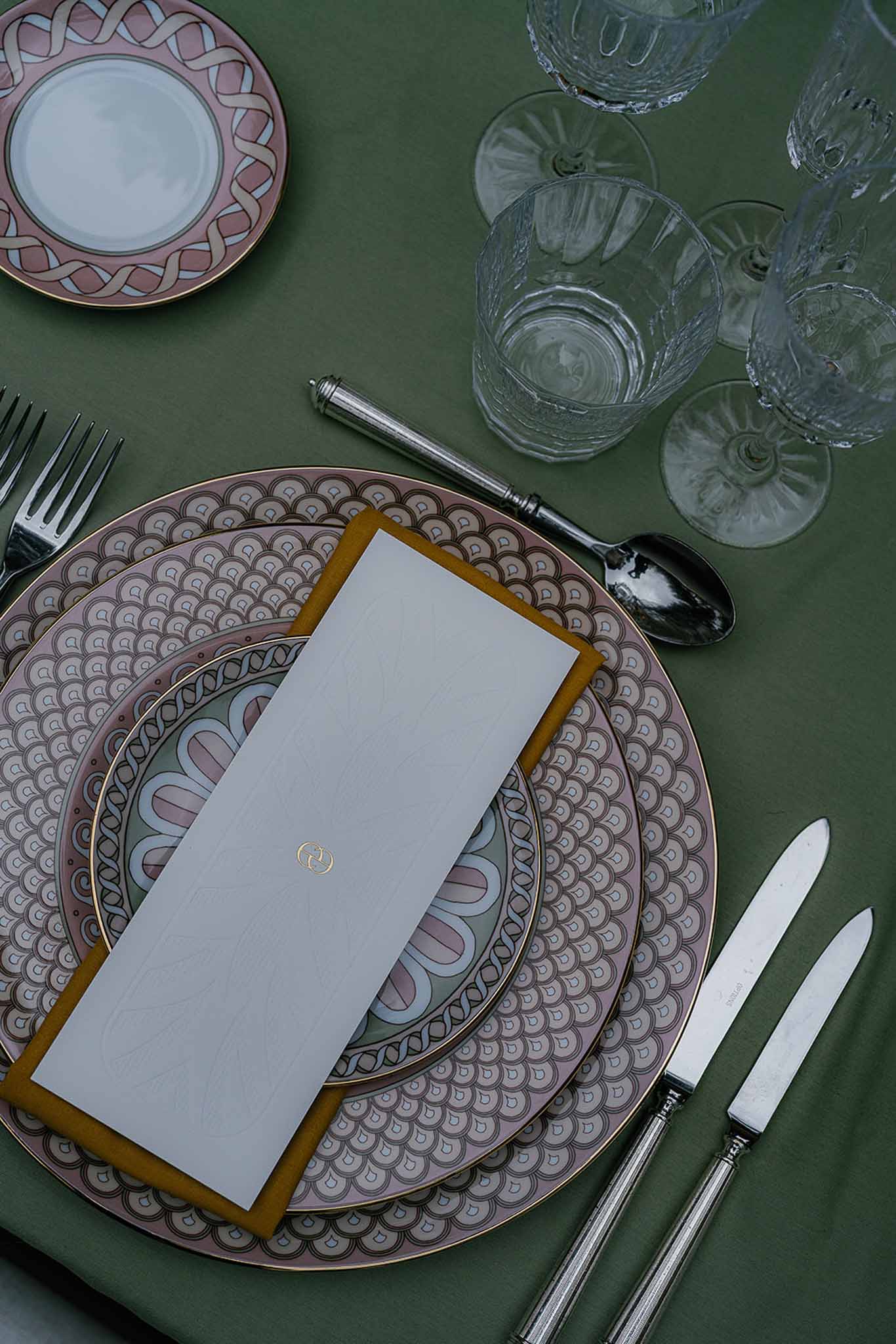 Place setting with Art Deco scallop plates mustard napkin and gold monogram menu on green linen